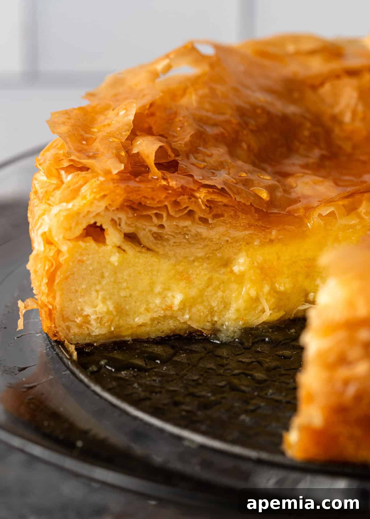Side view of a beautifully baked filo custard pie, with one slice removed to reveal the rich, creamy custard inside and the crisp, golden layers.