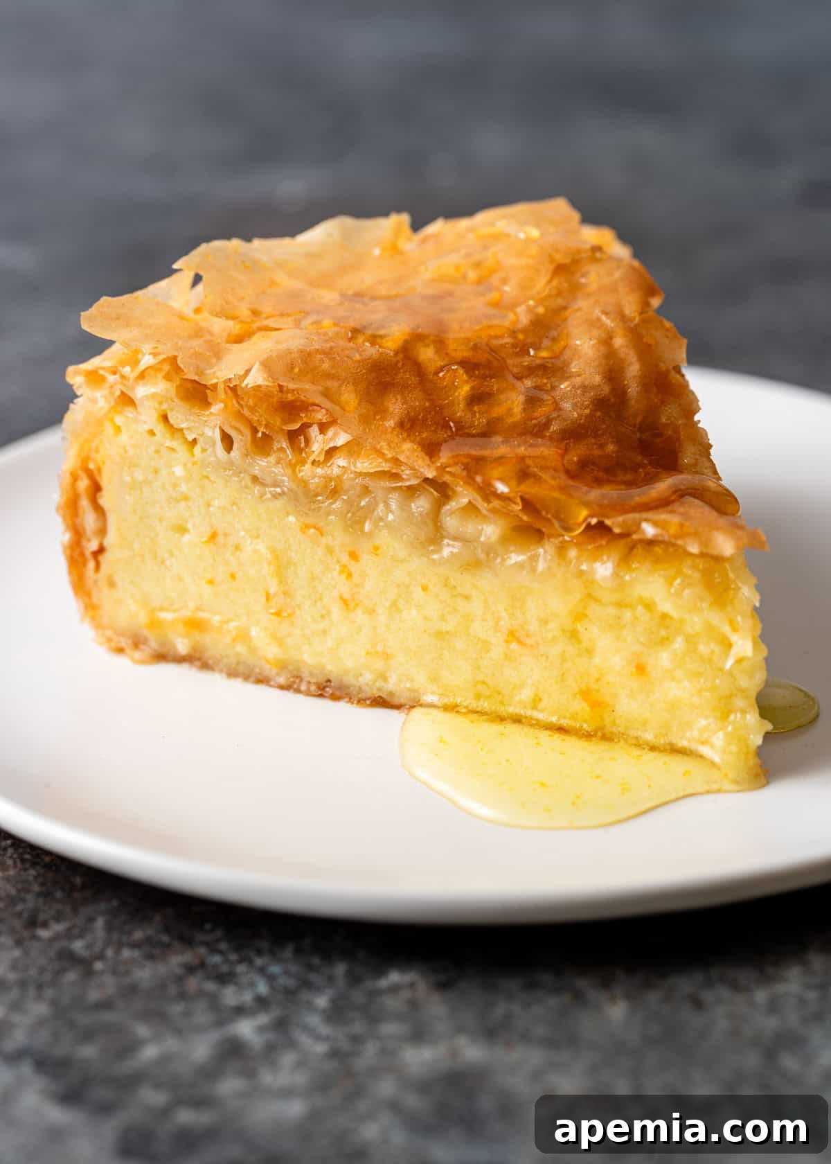 Close-up side view of a slice of Greek filo custard pie, showcasing the luscious, creamy semolina filling and crisp layers of golden pastry.
