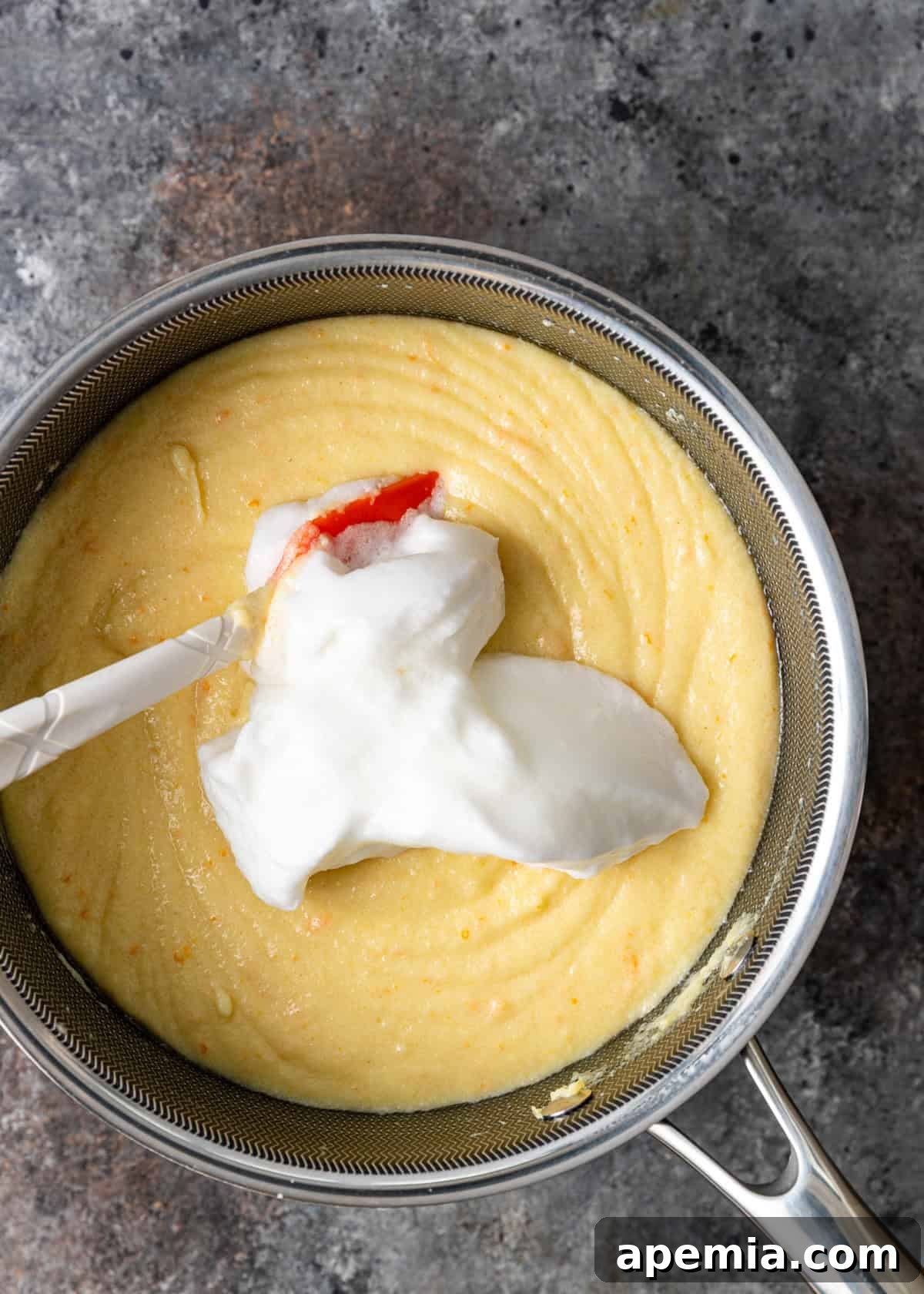 Overhead process shot capturing the moment whipped cream is carefully added to the warm semolina custard base, enhancing its texture.