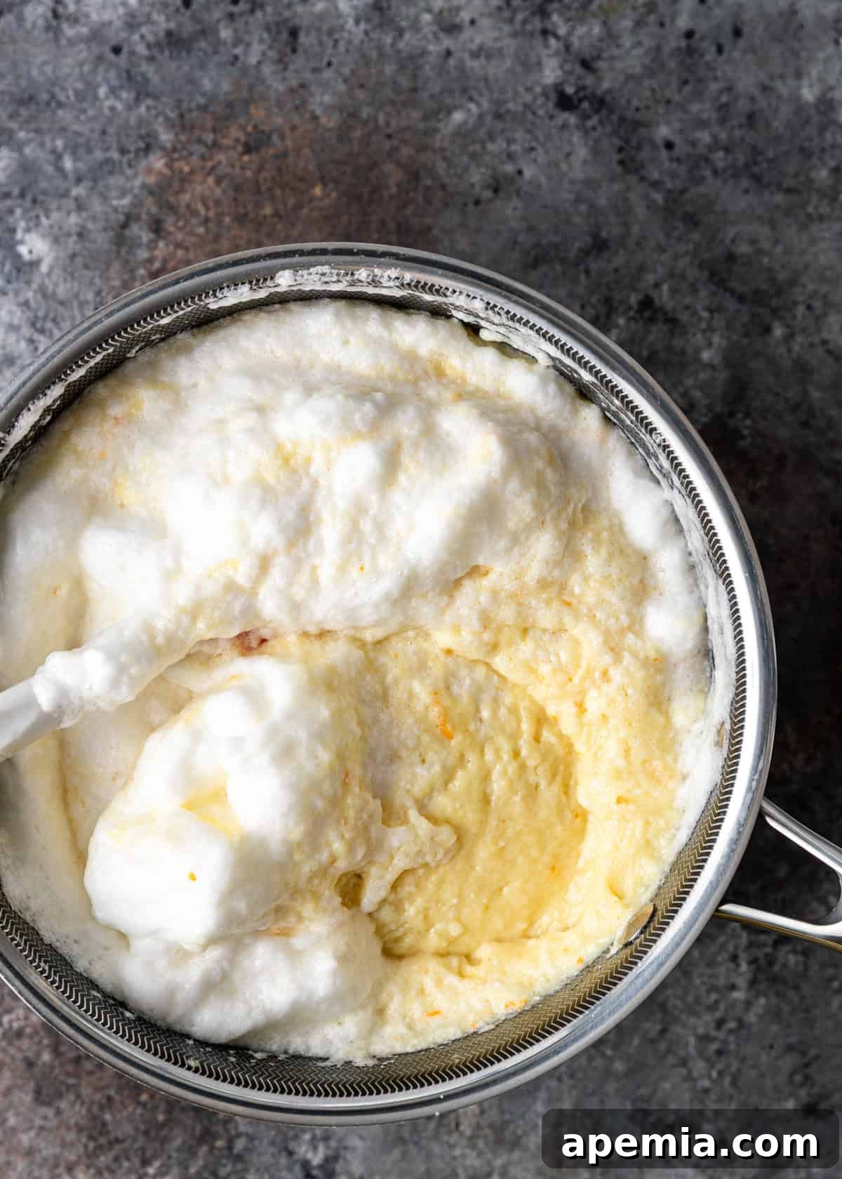 Overhead process shot showing the gentle mixing of whipped cream into the semolina custard, ensuring a smooth and airy consistency for the Galaktoboureko.