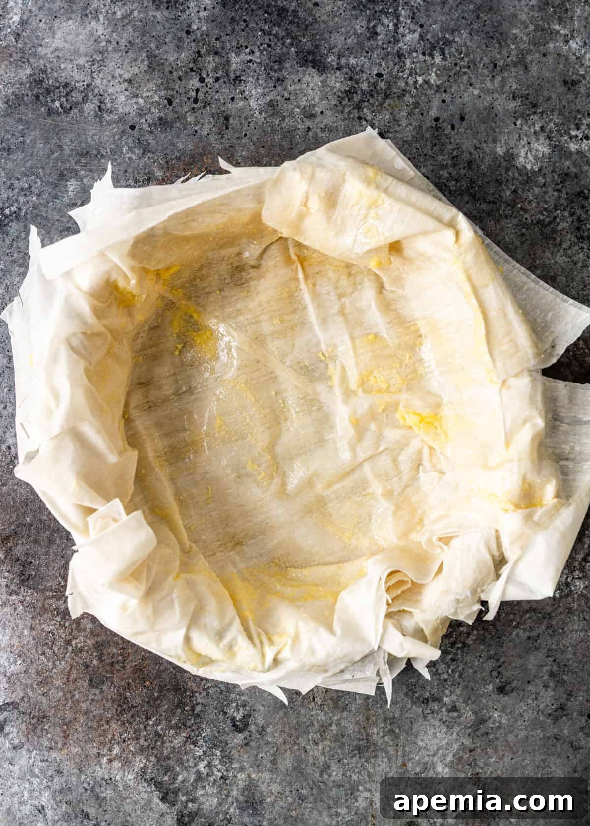 Overhead process shot demonstrating the careful arrangement of delicate filo sheets in an overlapping pattern within a springform pan.