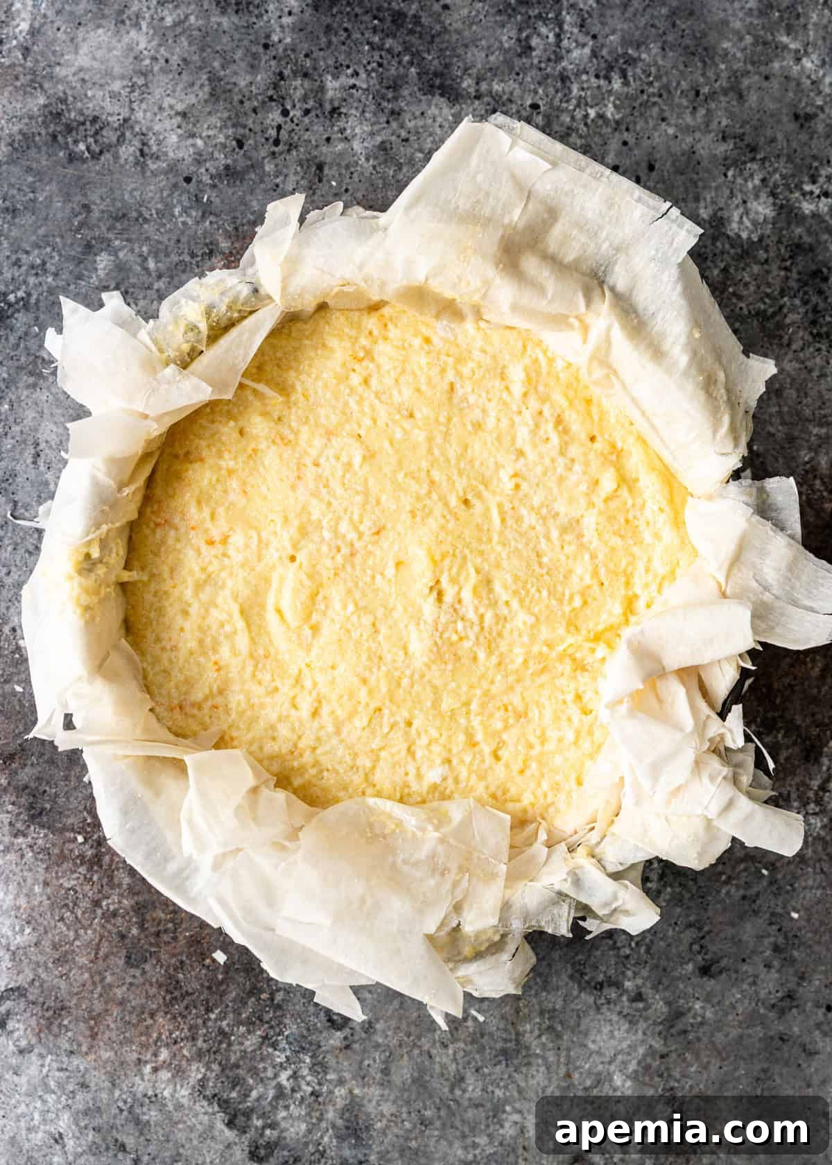 Overhead process shot showing the smooth semolina custard filling poured evenly over the base layers of filo sheets in a springform pan.