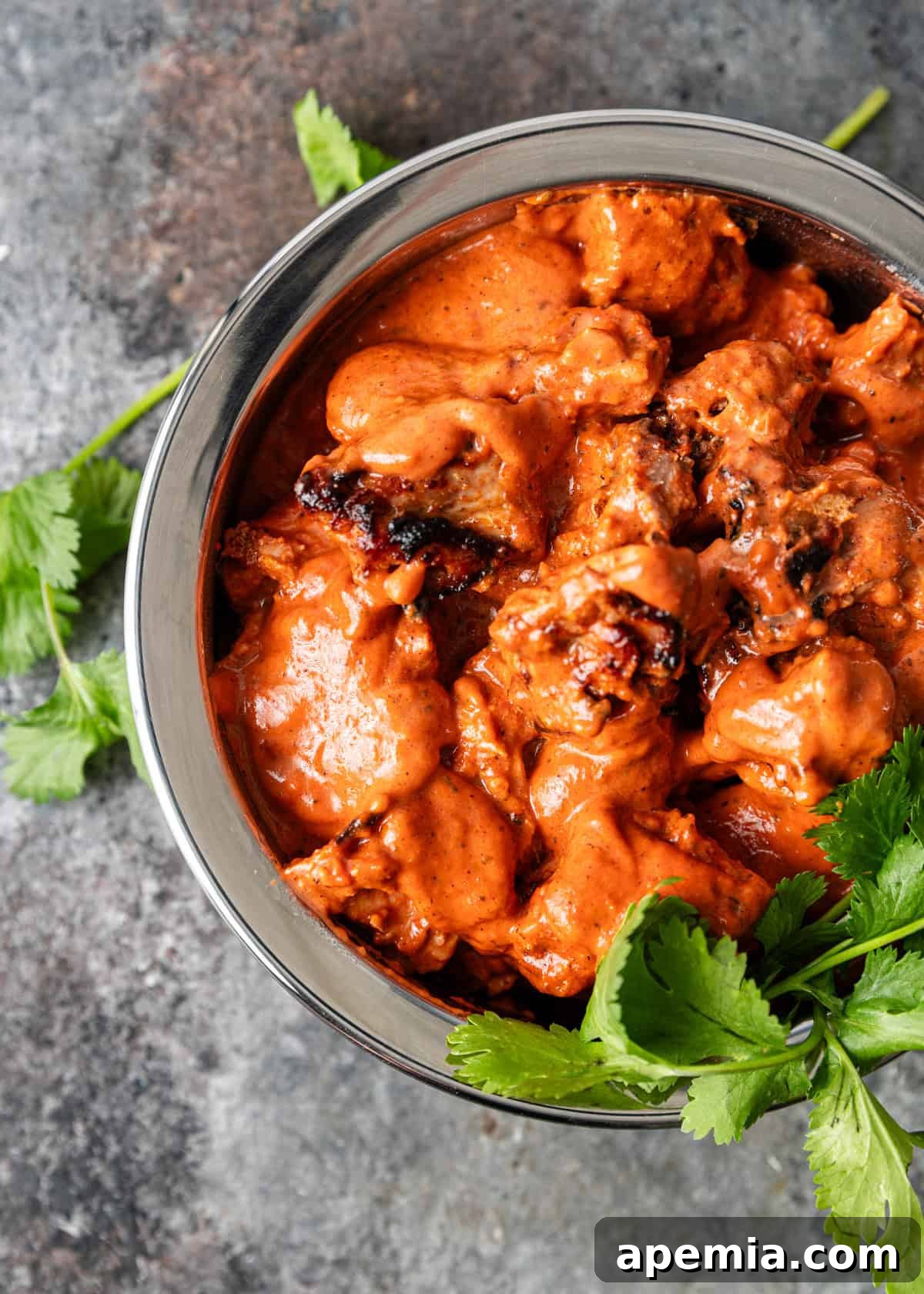 A glistening serving of ruby chicken curry in a silver dish, ready to be enjoyed.