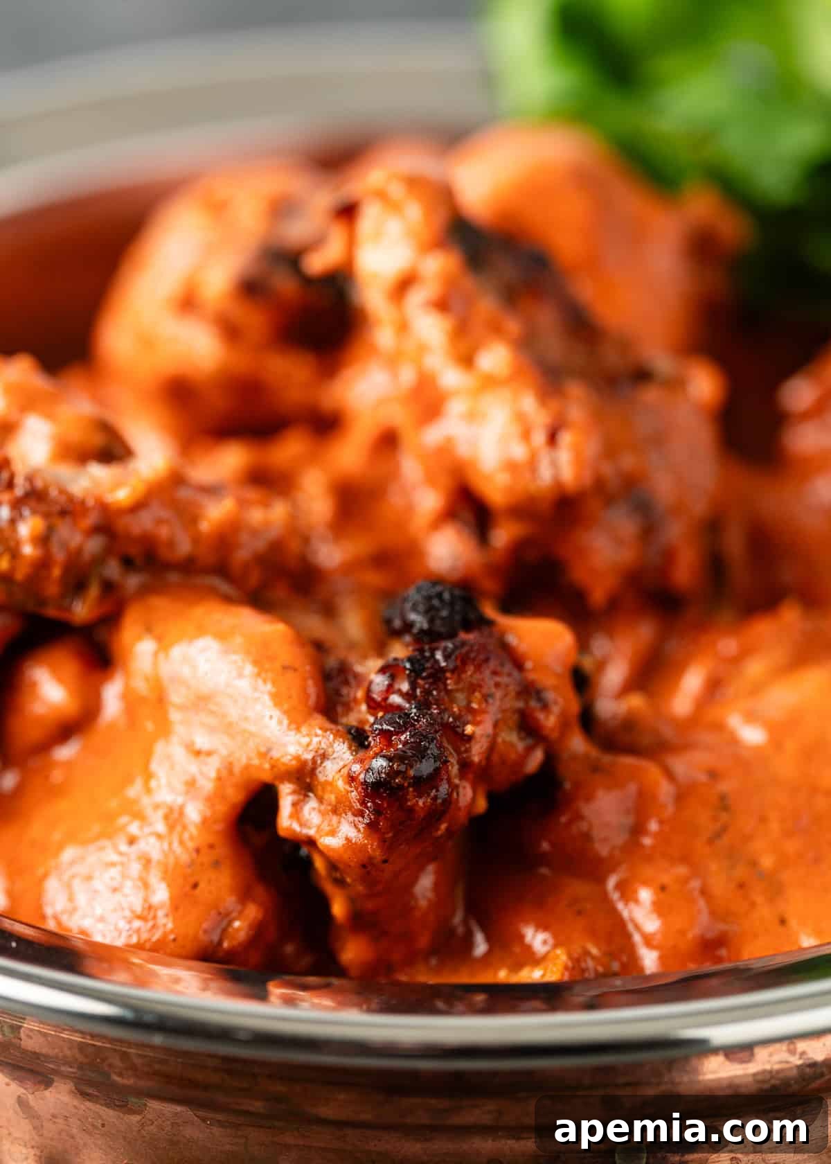 Extreme close-up shot of saucy ruby chicken in a skillet, showcasing the rich texture and deep red color.