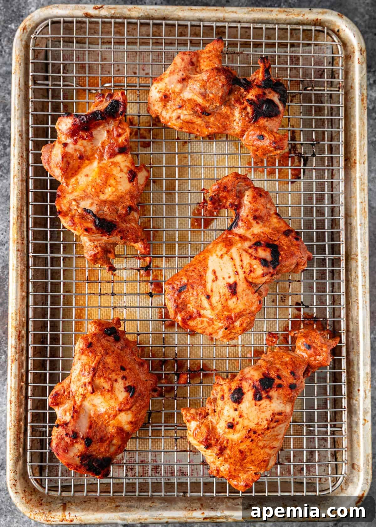 Broiled chicken thighs, golden and slightly charred, cooling on a wire rack after being cooked for the curry.