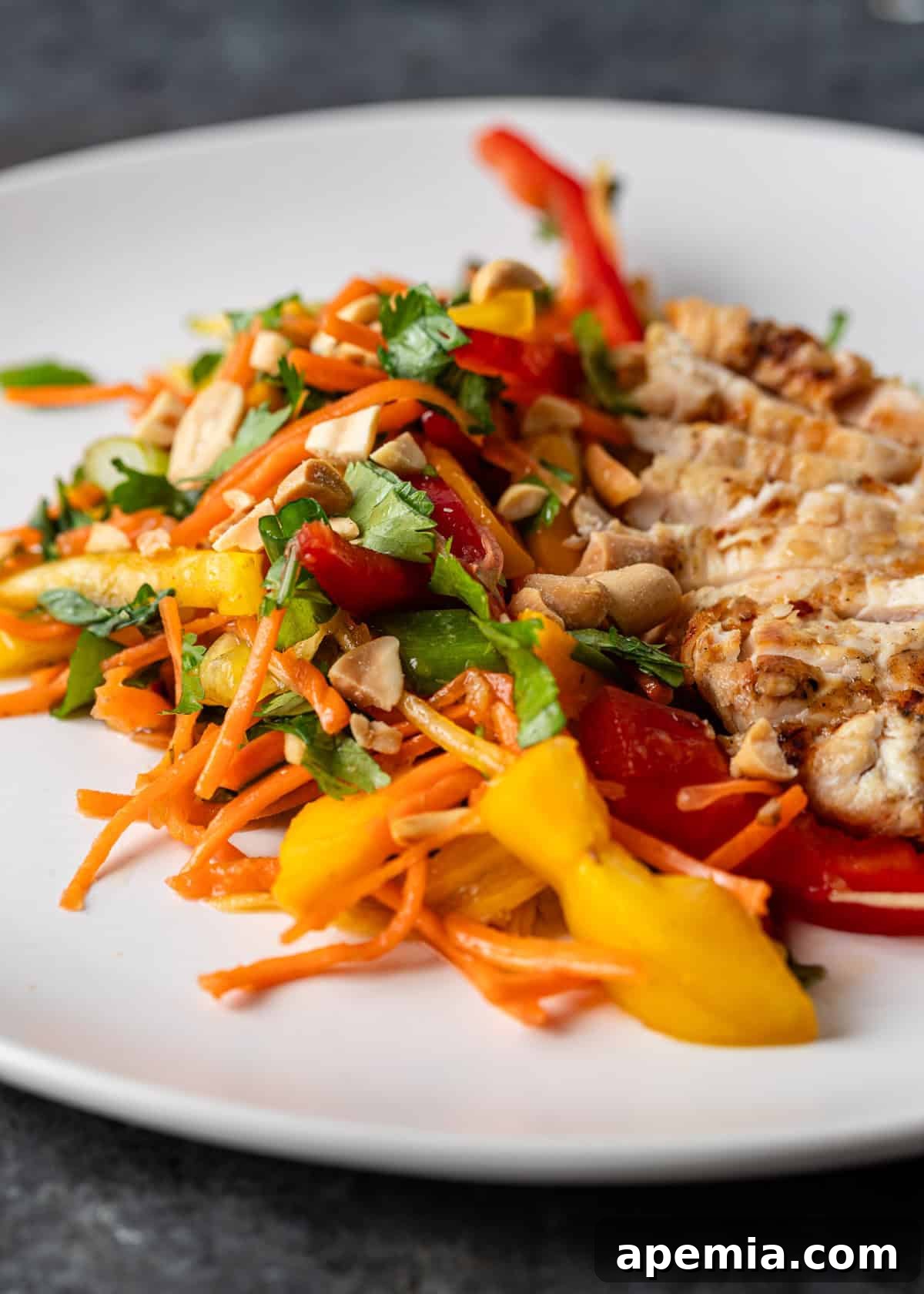 Closeup of chicken mango salad adorned with fresh fruit, vegetables, nuts, and herbs