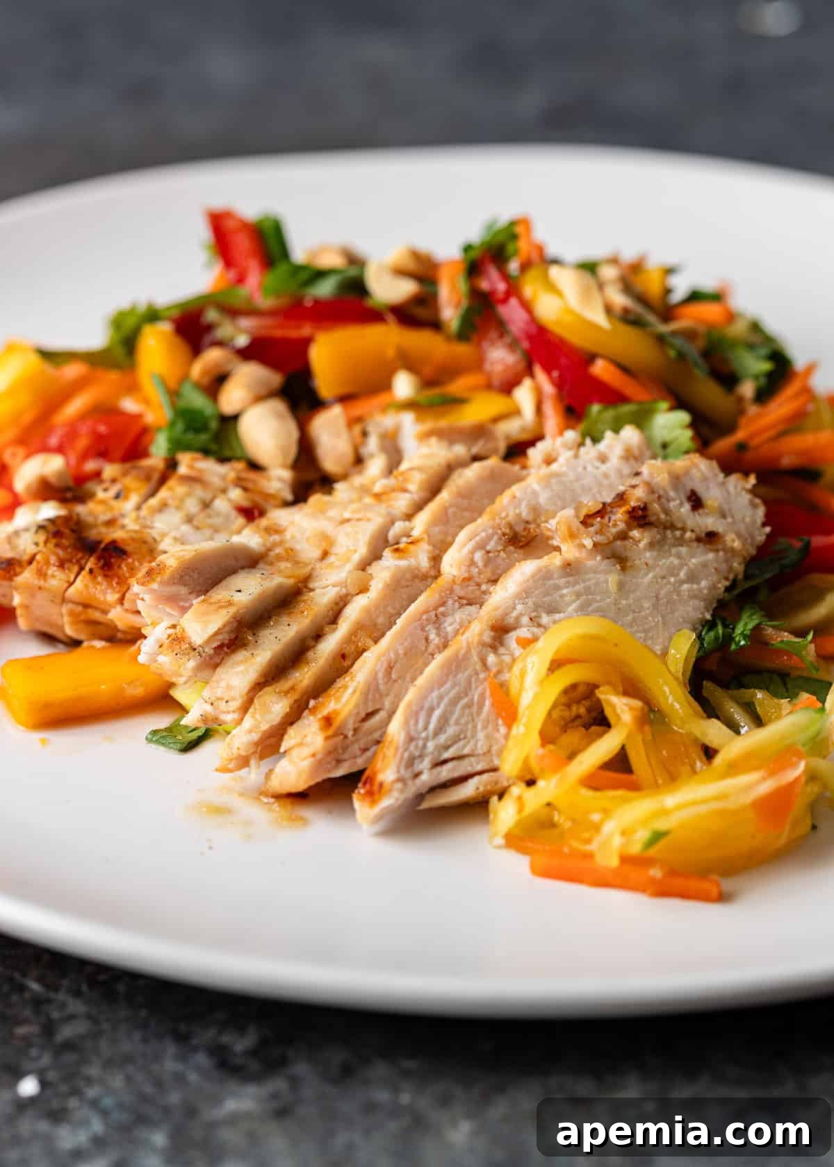 Closeup of perfectly sliced chicken arranged on top of the colorful fruits and veggies of the salad