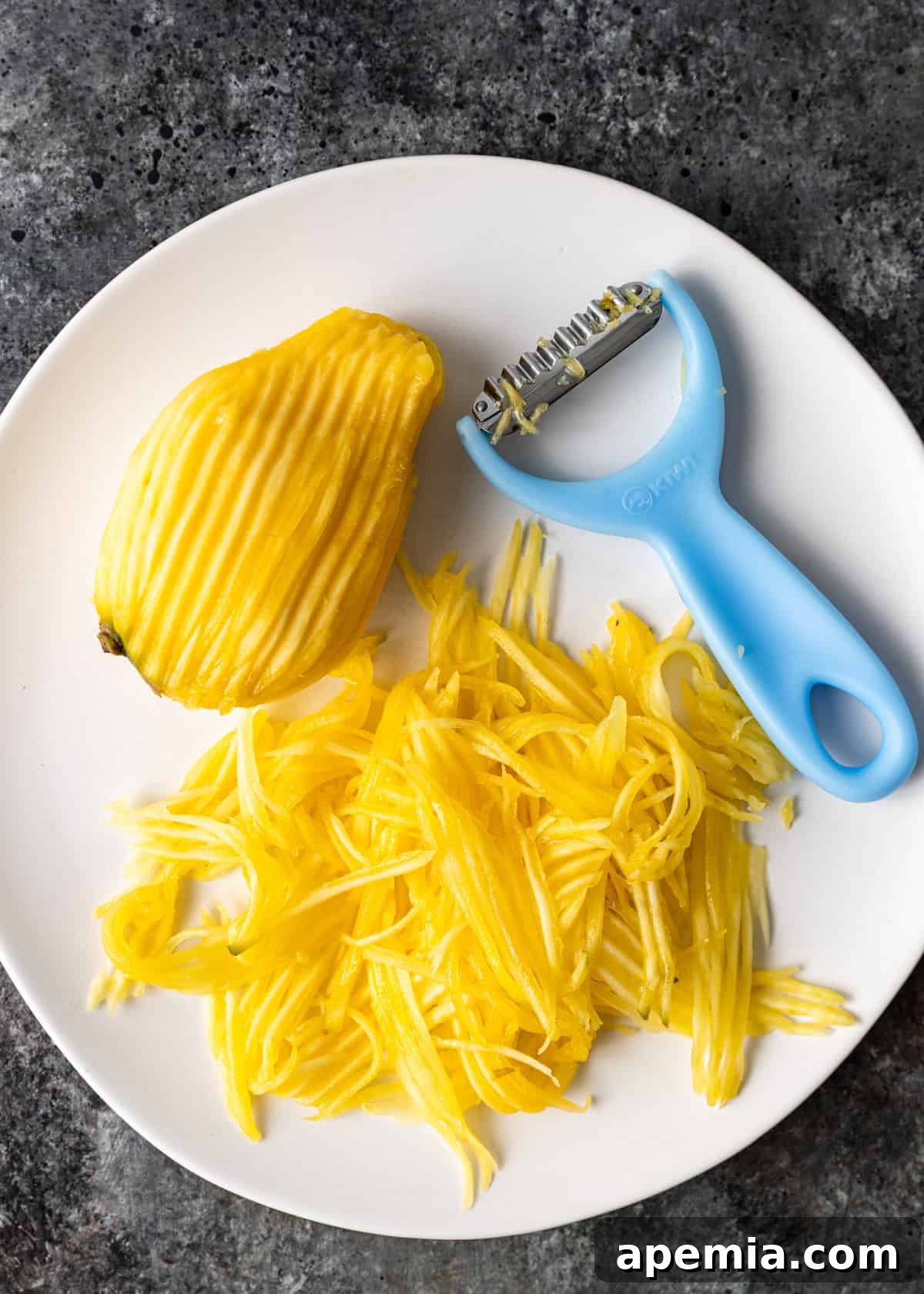Overhead shot of shredded mango with a shredding tool on a white plate