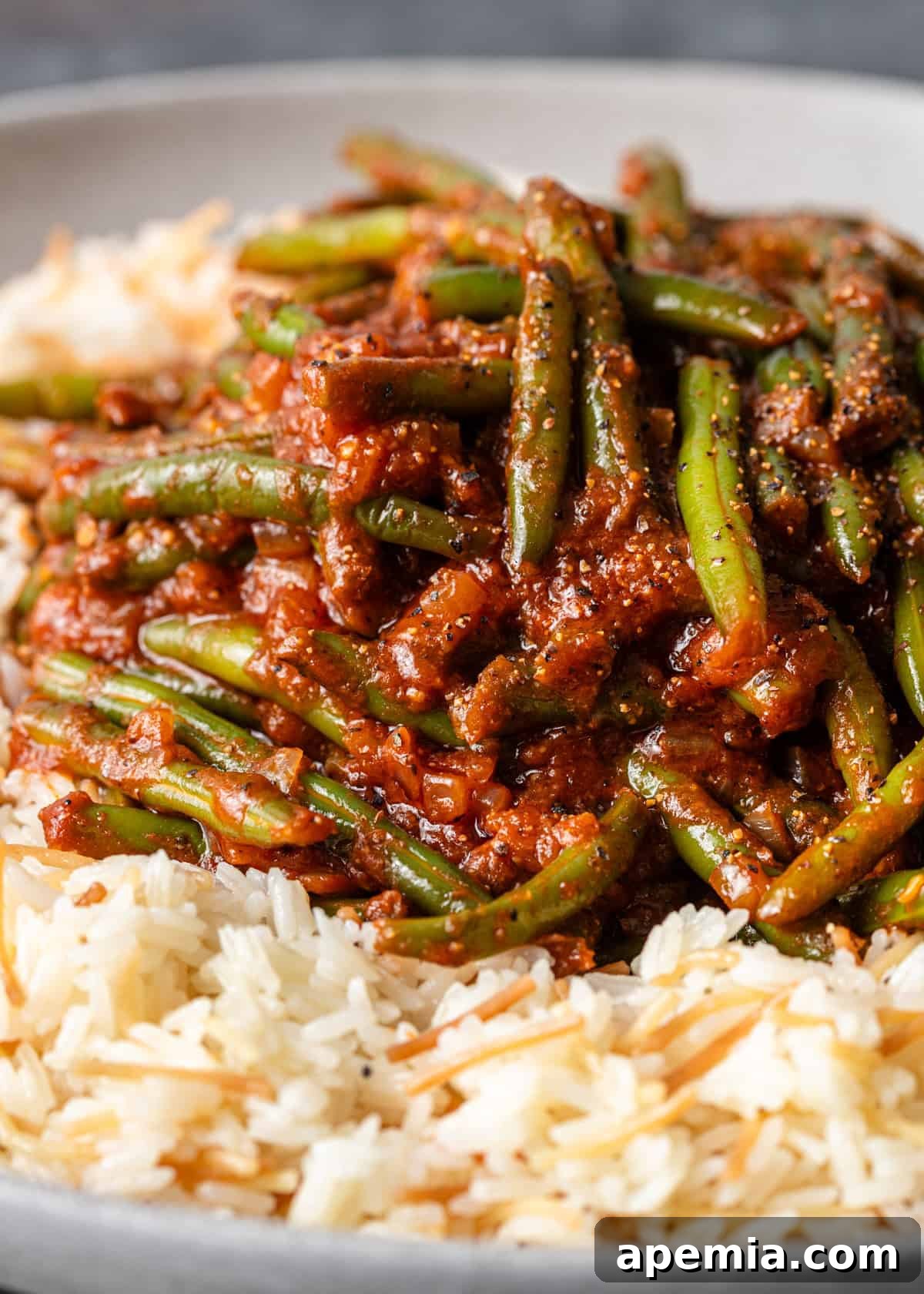 A close-up view of creamy Fasooliya (Egyptian stewed green beans) simmering in a rich, red tomato sauce, served over perfectly cooked rice.