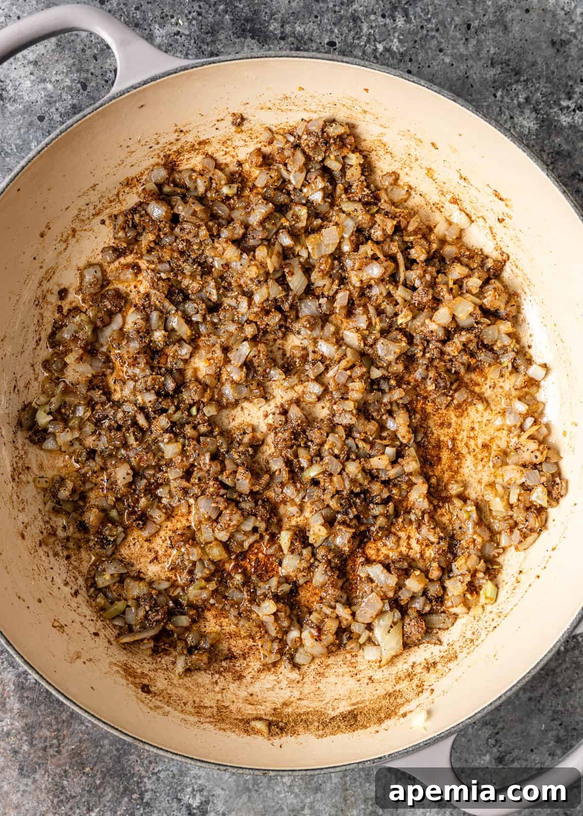 An overhead process shot showing diced onions and aromatic seasonings lightly sautéing in a skillet, filling the kitchen with a wonderful aroma.