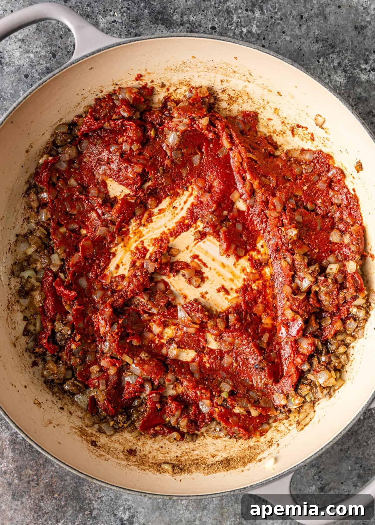 A process shot from above, capturing onions, spices, and a dollop of rich tomato paste actively sautéing in a pan, deepening in color and flavor for the stewed green beans.