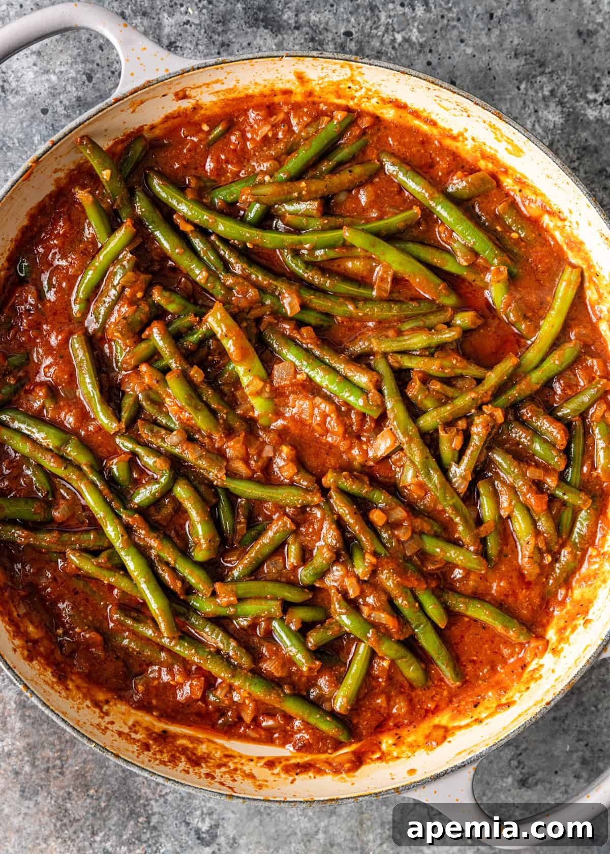 An overhead view of the Egyptian green bean stew, Fasooliya, gently simmering in a skillet, its rich tomato sauce bubbling and fragrant, promising a delicious meal.