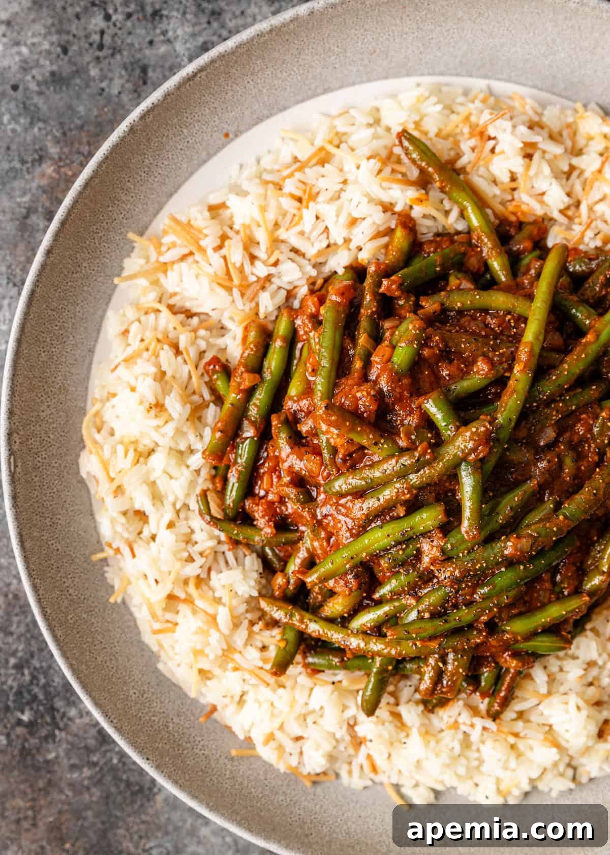 A generous serving of Egyptian Fasooliya (stewed green beans) delicately piled over a bed of fluffy vermicelli rice, creating a visually appealing and delicious meal.
