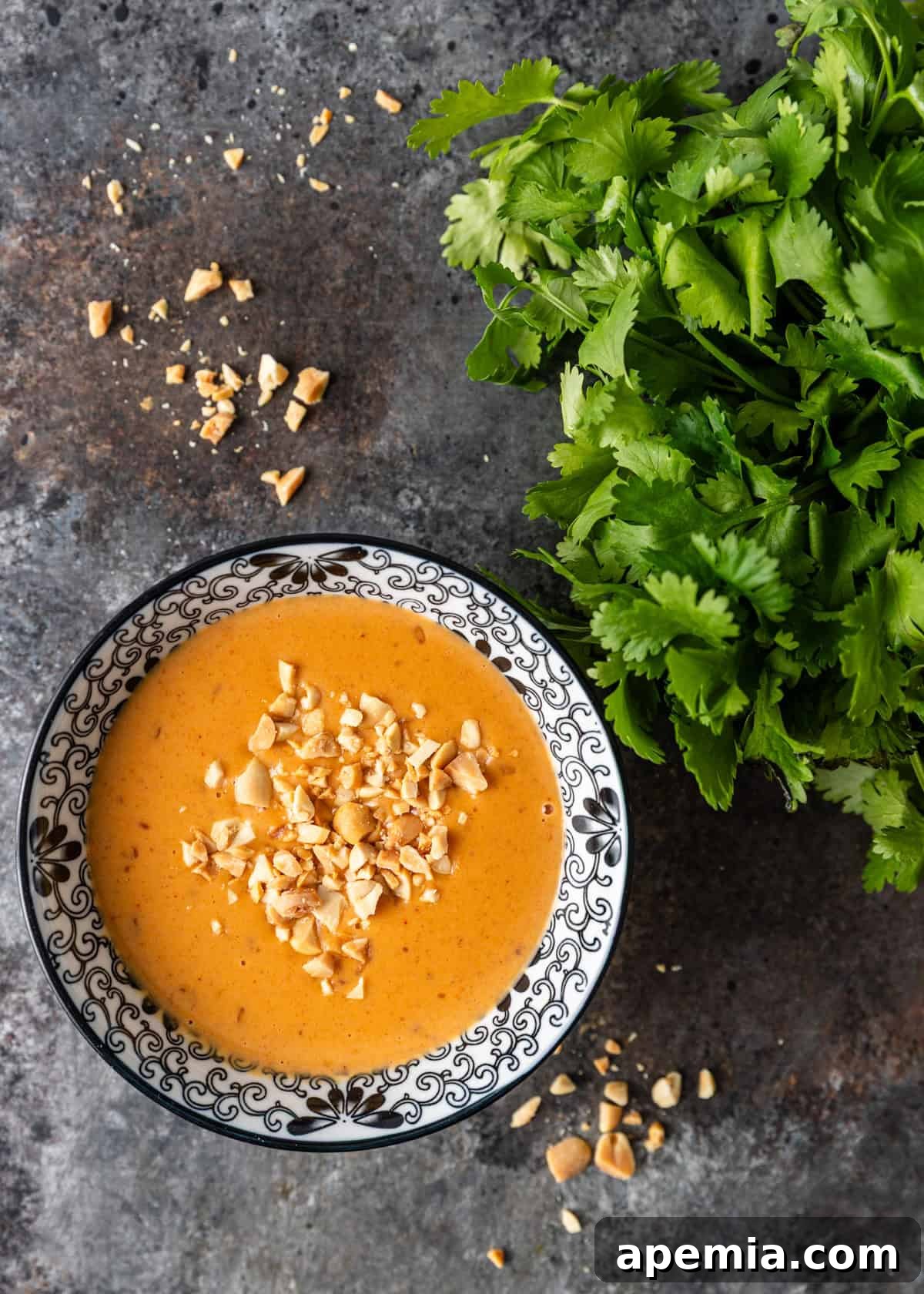 An overhead view displaying a small, elegant bowl of my homemade Thai peanut sauce recipe, elegantly topped with a delicate scattering of crushed nuts for visual appeal and added crunch.