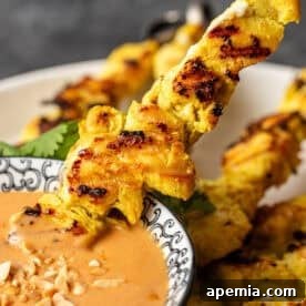 Close-up of perfectly grilled chicken satay skewers arranged on a white plate with a bowl of peanut dipping sauce.