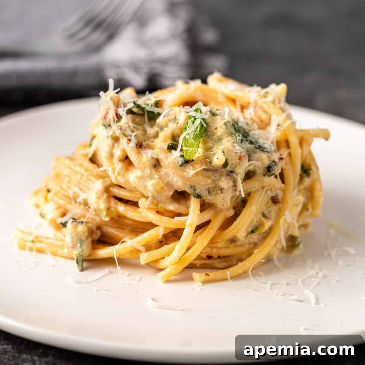Closeup side view: a serving of lemon zucchini pasta with fresh lemon slices and mint leaves on a plate