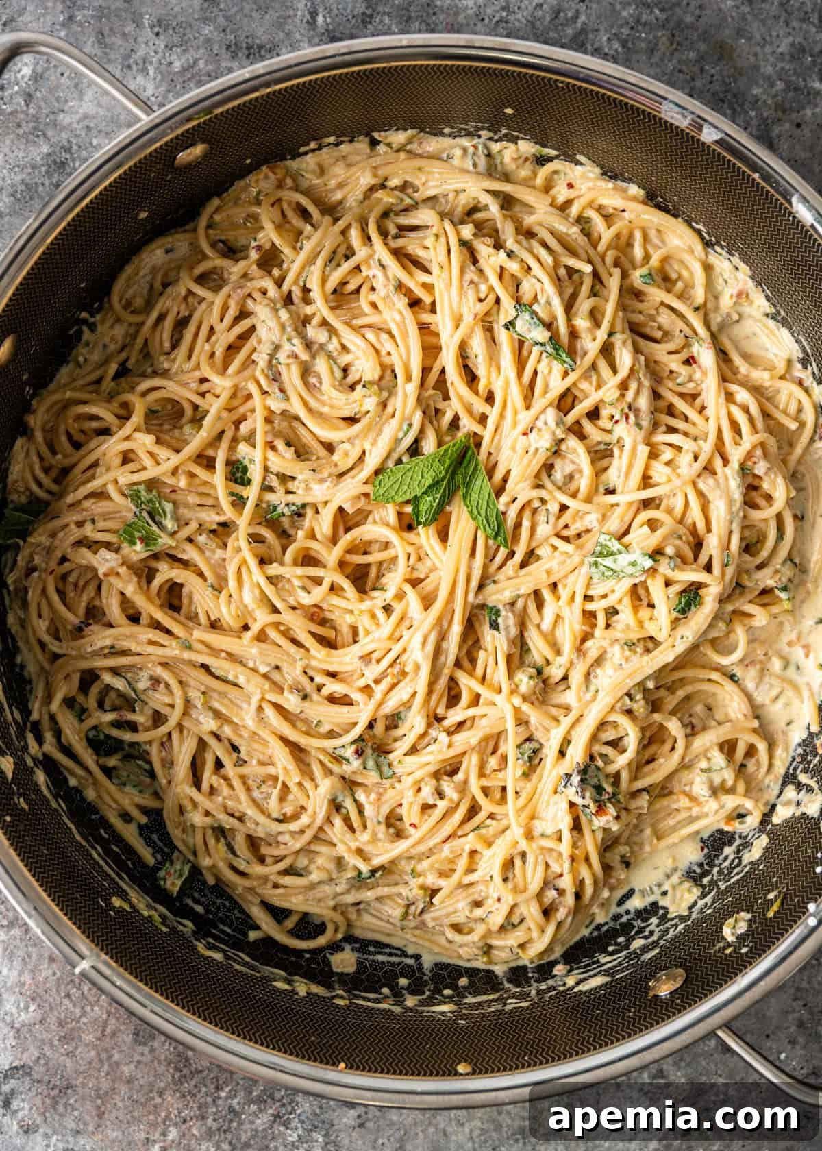Overhead view: cooked and ready-to-serve lemon zucchini pasta recipe in a skillet, garnished with fresh mint leaves