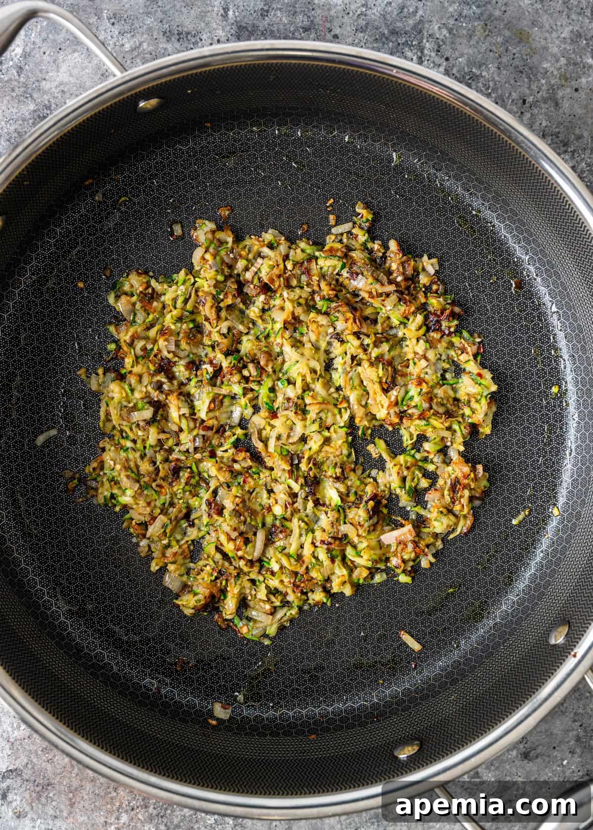 Overhead process shot: the zucchini, shallots, and garlic mixture has reduced significantly and caramelized slightly in the skillet