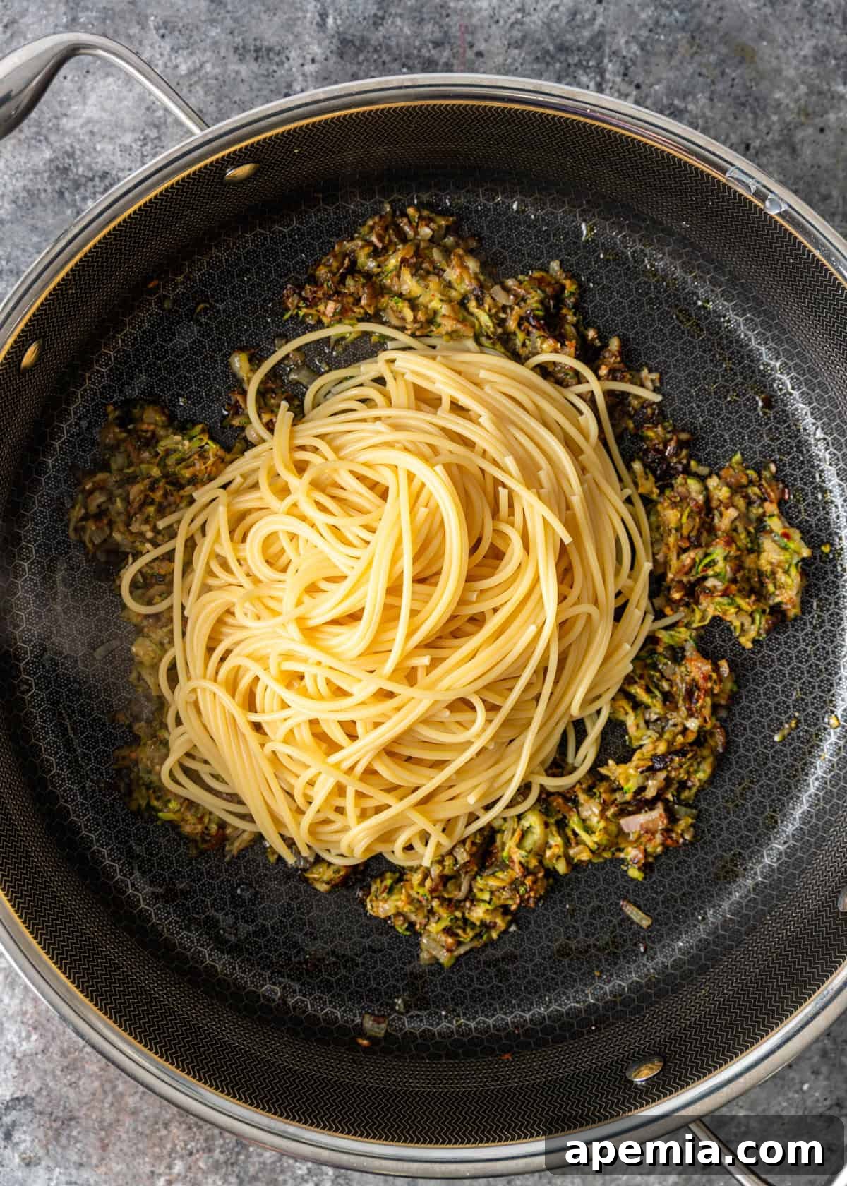 Overhead process shot: adding freshly cooked spaghetti directly to the skillet containing the zucchini sauce