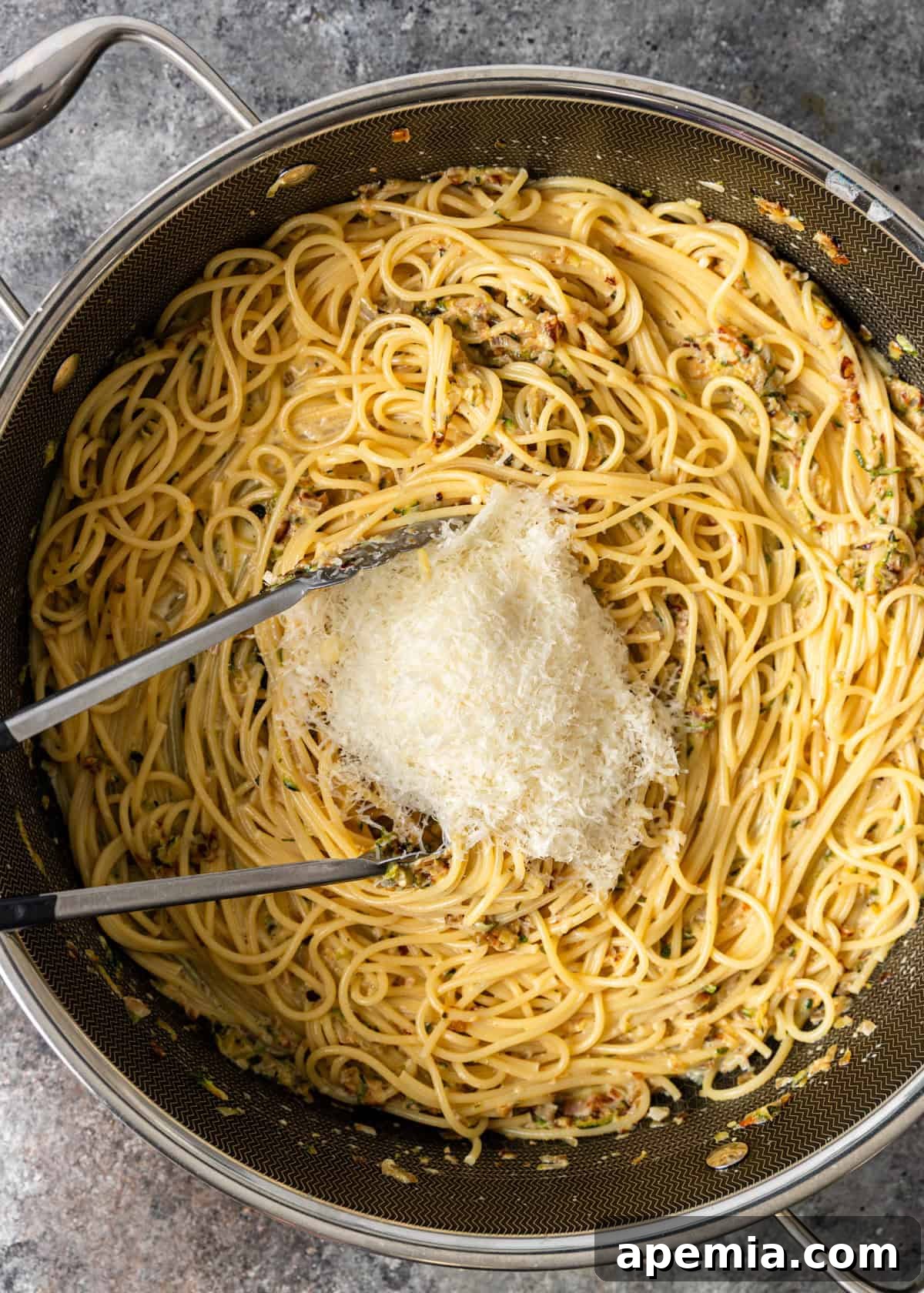 Overhead process shot: adding grated Parmesan cheese to the skillet with the zucchini pasta, stirring to create a creamy sauce