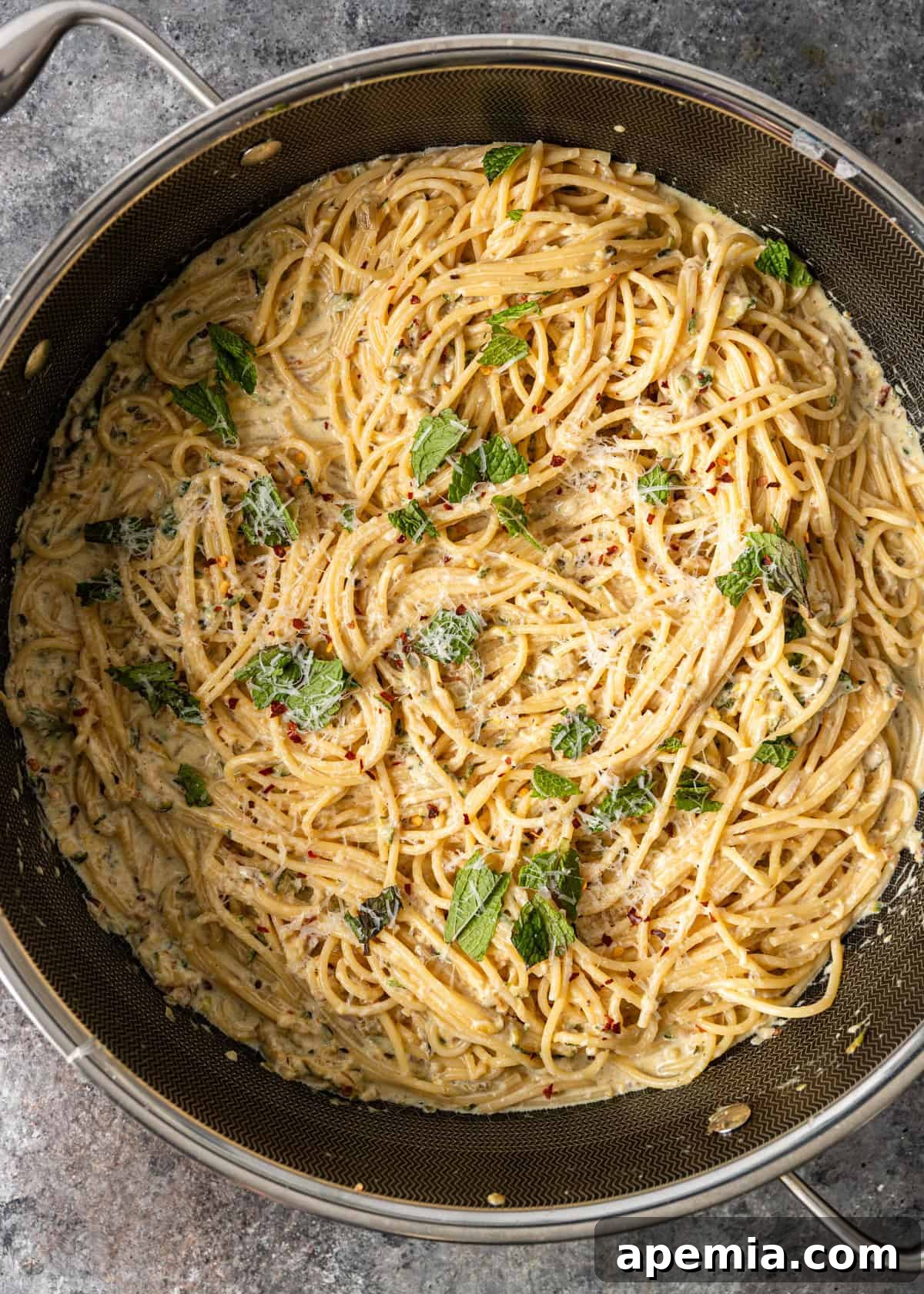 Overhead process shot: lemon zucchini pasta recipe in a skillet, topped with fresh mint leaves and ready to be served