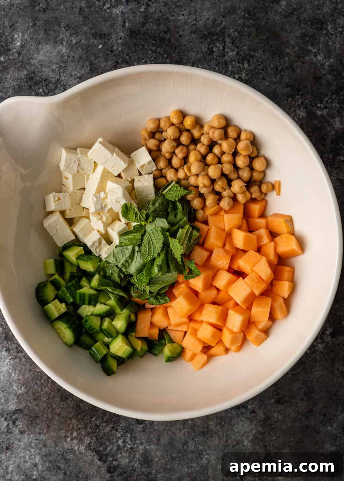 overhead: melon salad ingredients in a large bowl before mixing, showing colorful components