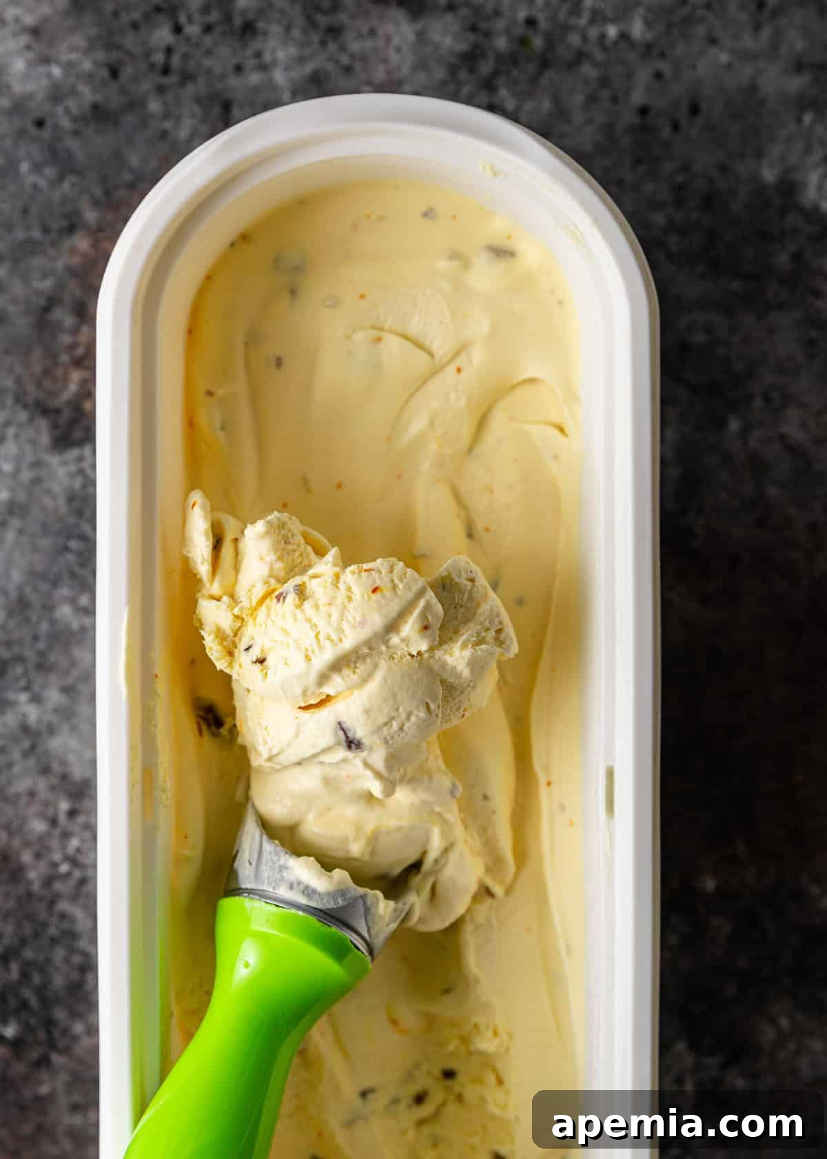 Overhead view: Scooping out a generous portion of creamy pistachio and saffron ice cream from its container.