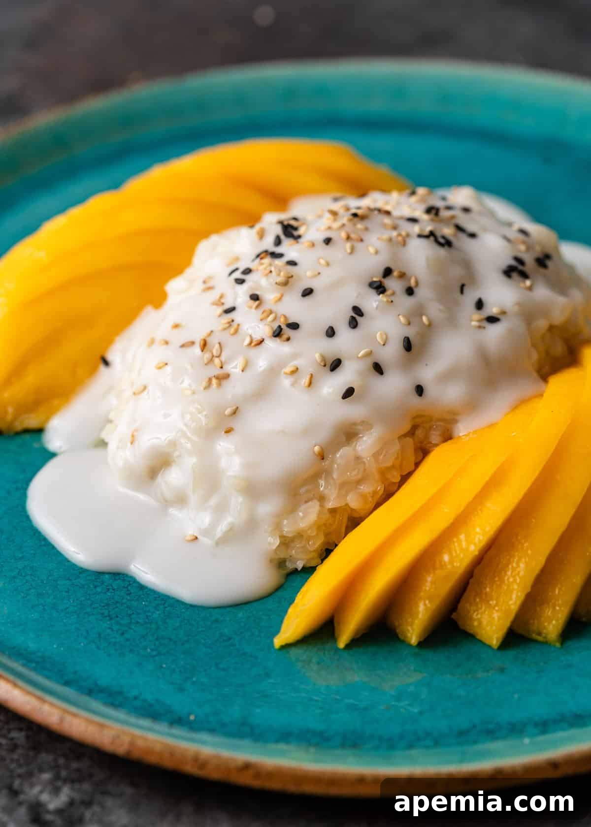 A generous serving of homemade mango sticky rice garnished with sesame seeds on a round blue plate