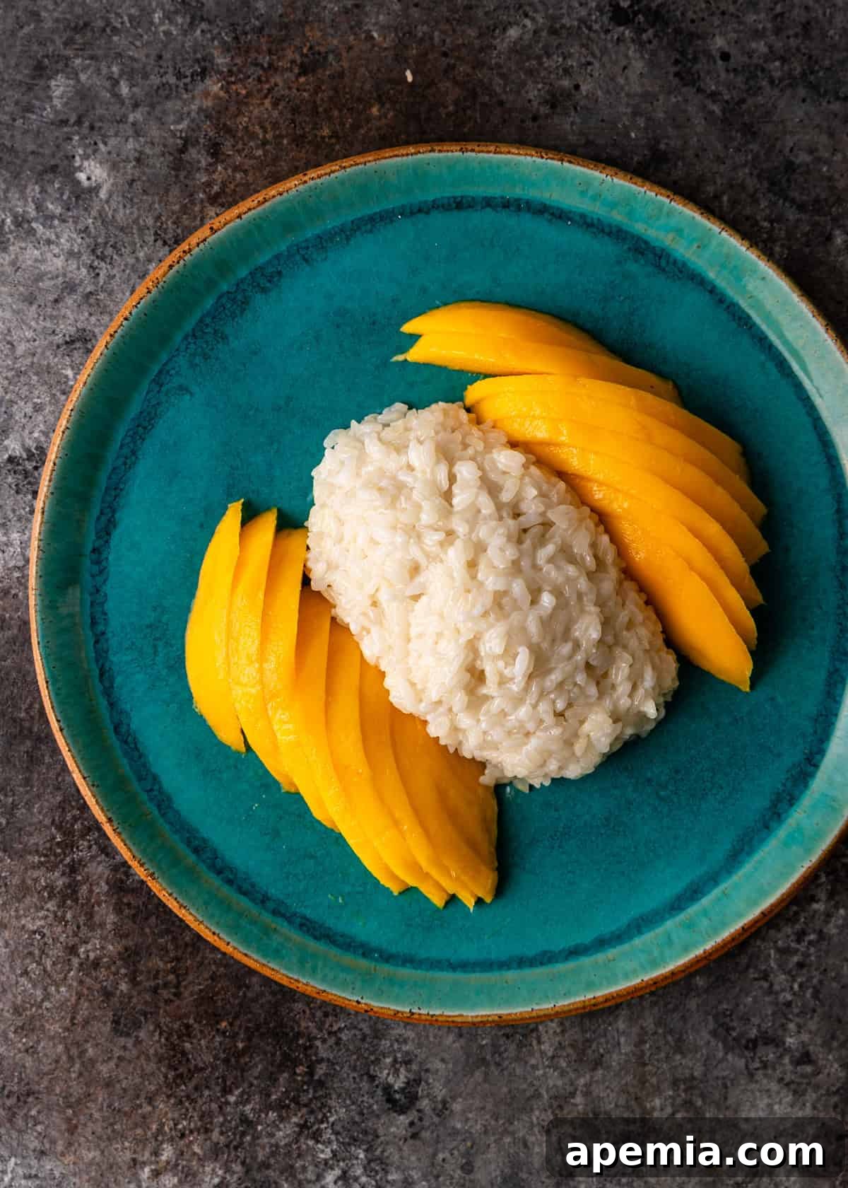 Overhead view: sticky rice and fresh mango slices arranged on a plate before the coconut sauce is added