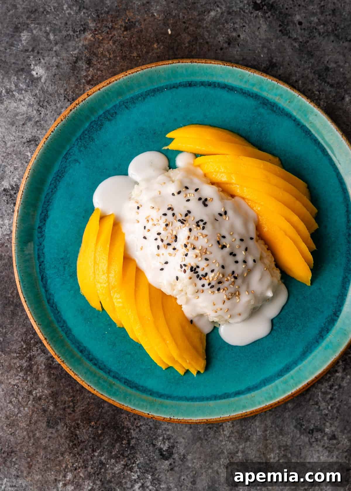 Overhead view: fully assembled mango sticky rice with coconut sauce generously drizzled over the rice and mango
