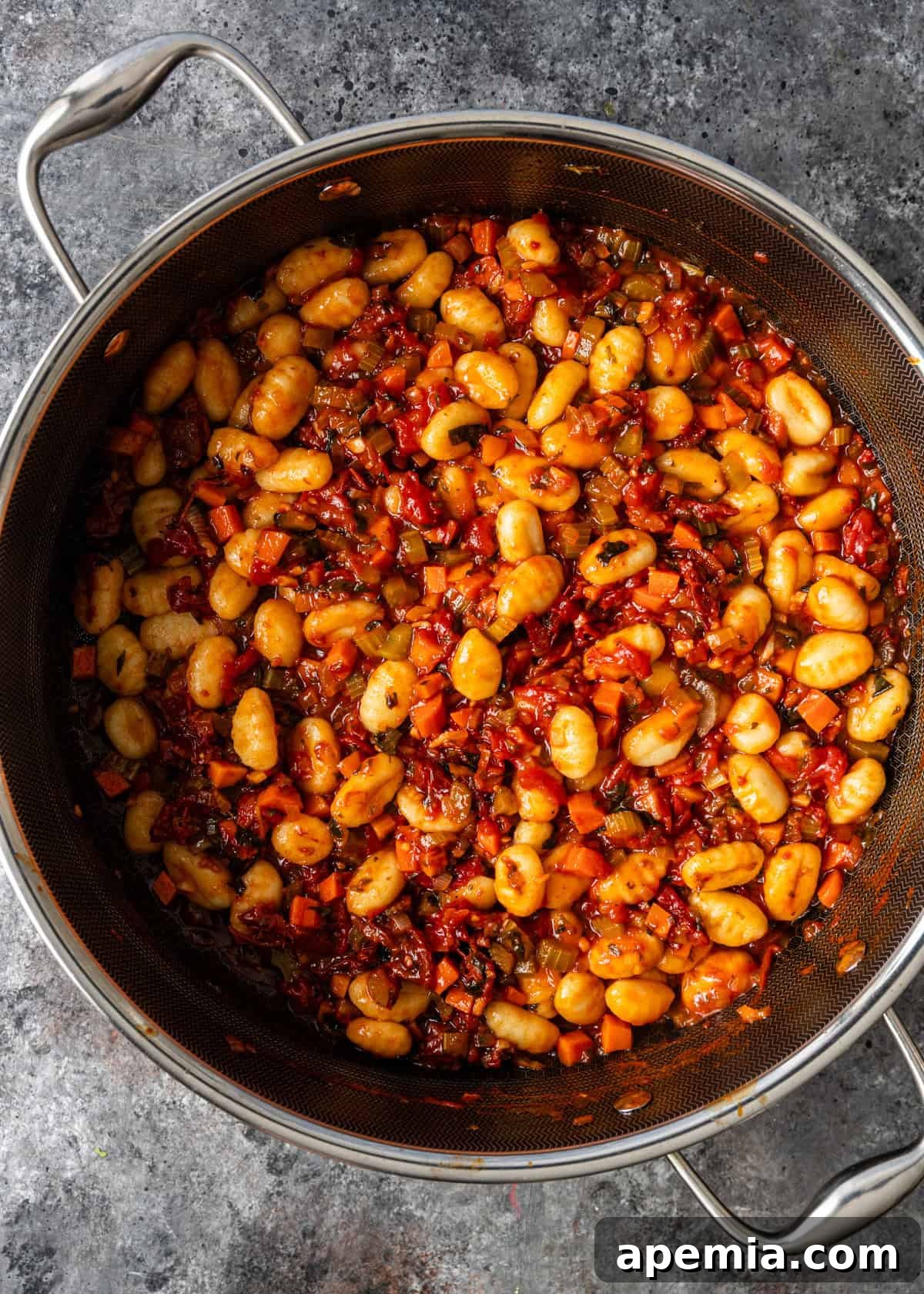 overhead process shot: cooked gnocchi added to the ragù skillet, being stirred to coat
