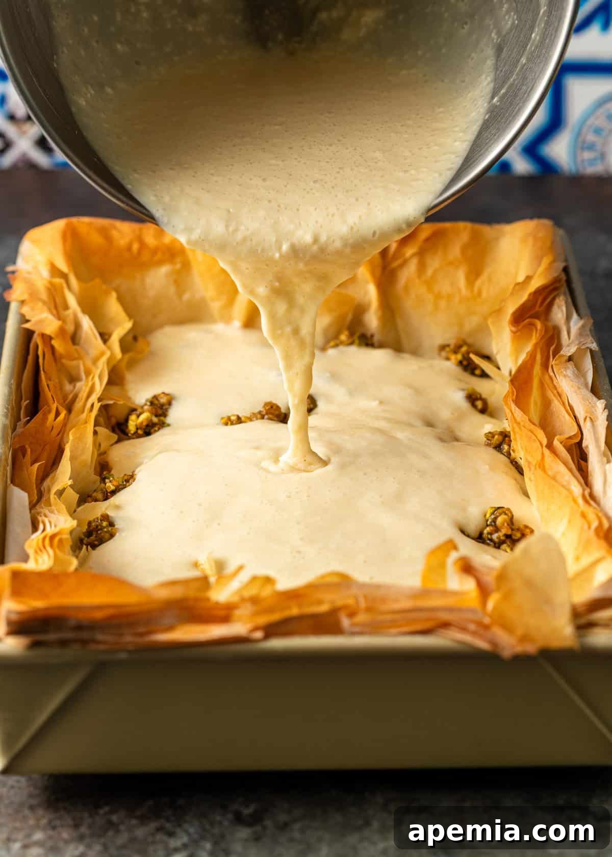 overhead process shot: mixing bowl over top pouring cheesecake mixture into baked baklava