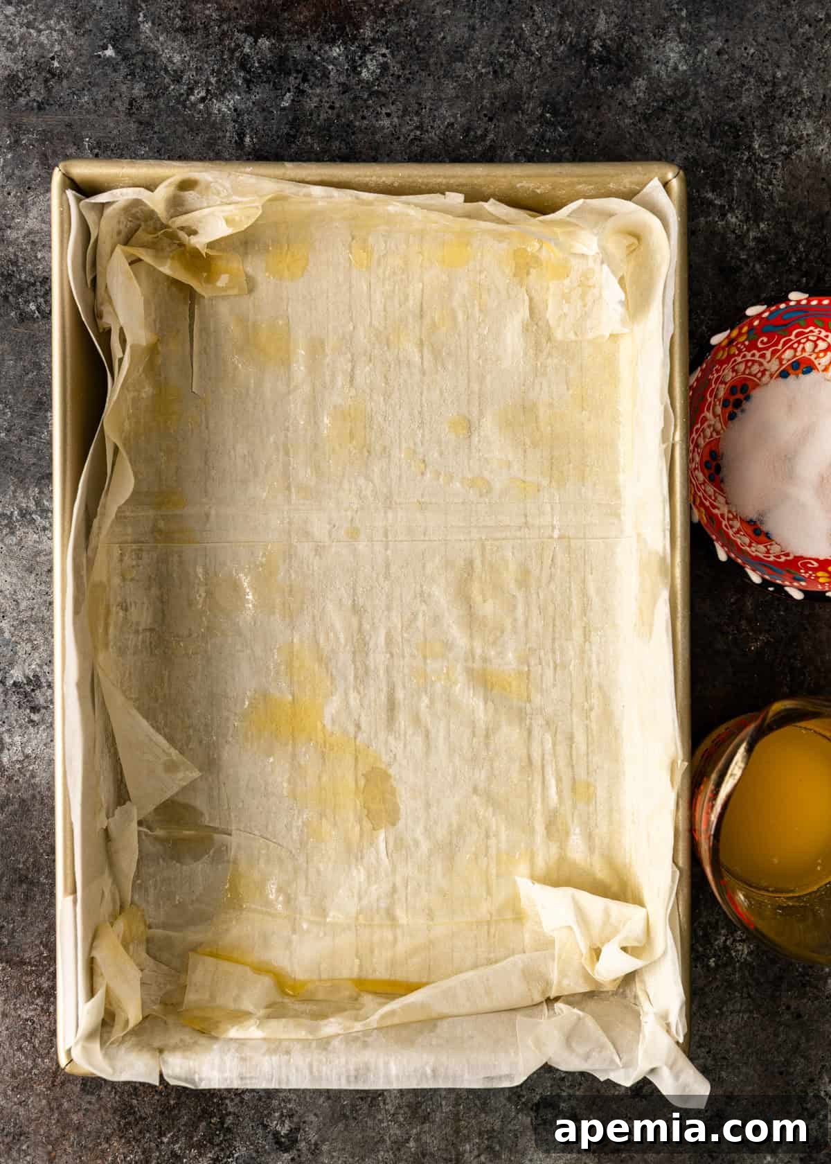 overhead process shot: phyllo dough in sheet pan with butter and sugar on top