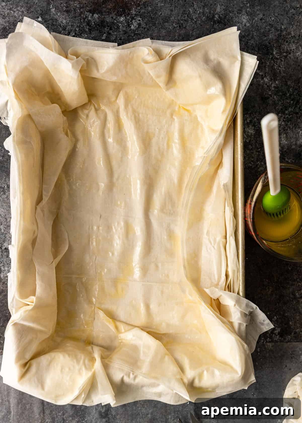 overhead process shot: several layers of phyllo dough in sheet pan with butter and sugar on top
