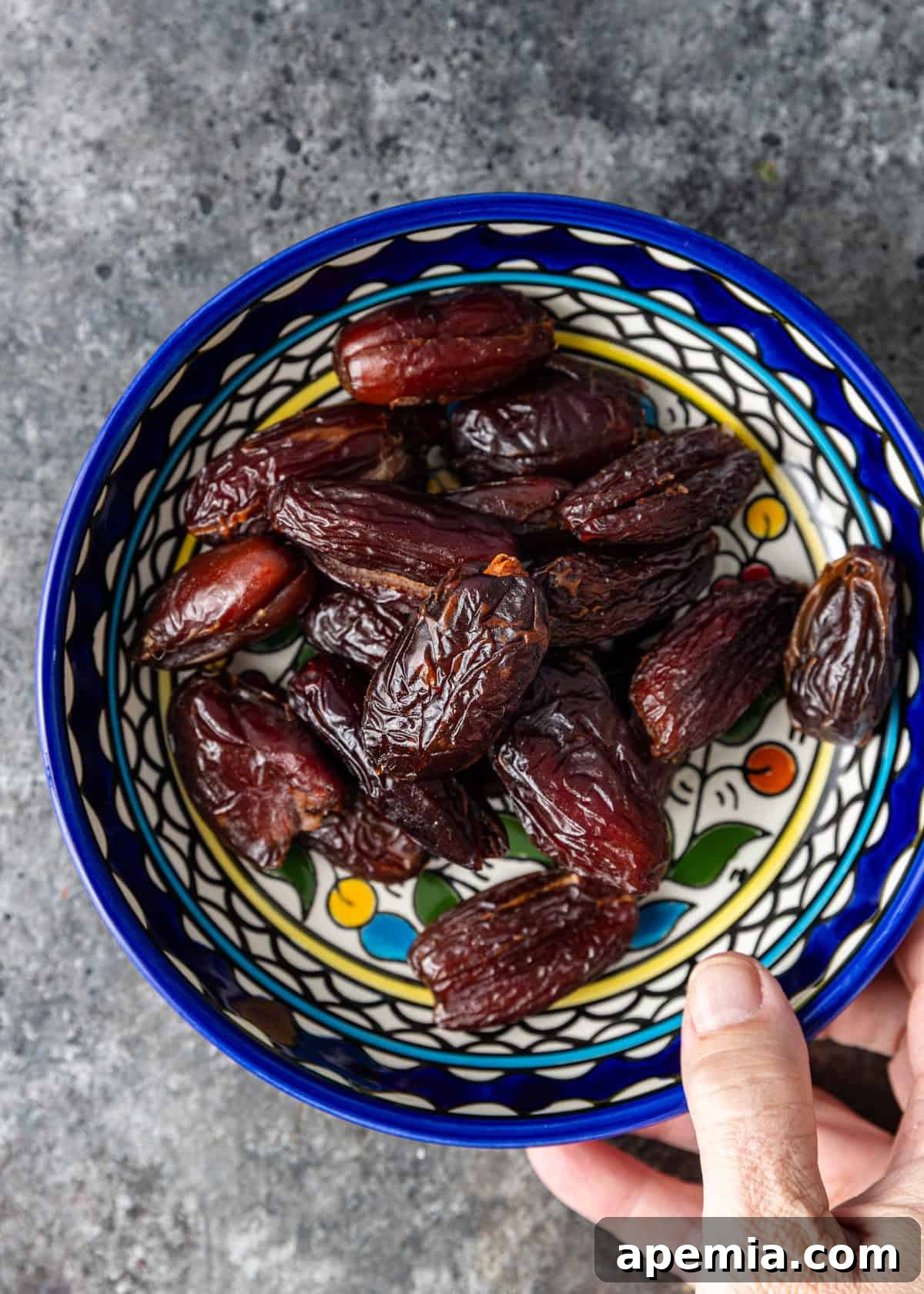 Overhead view: a rustic bowl filled with plump, dark Medjool dates resting on a warm-toned kitchen counter.