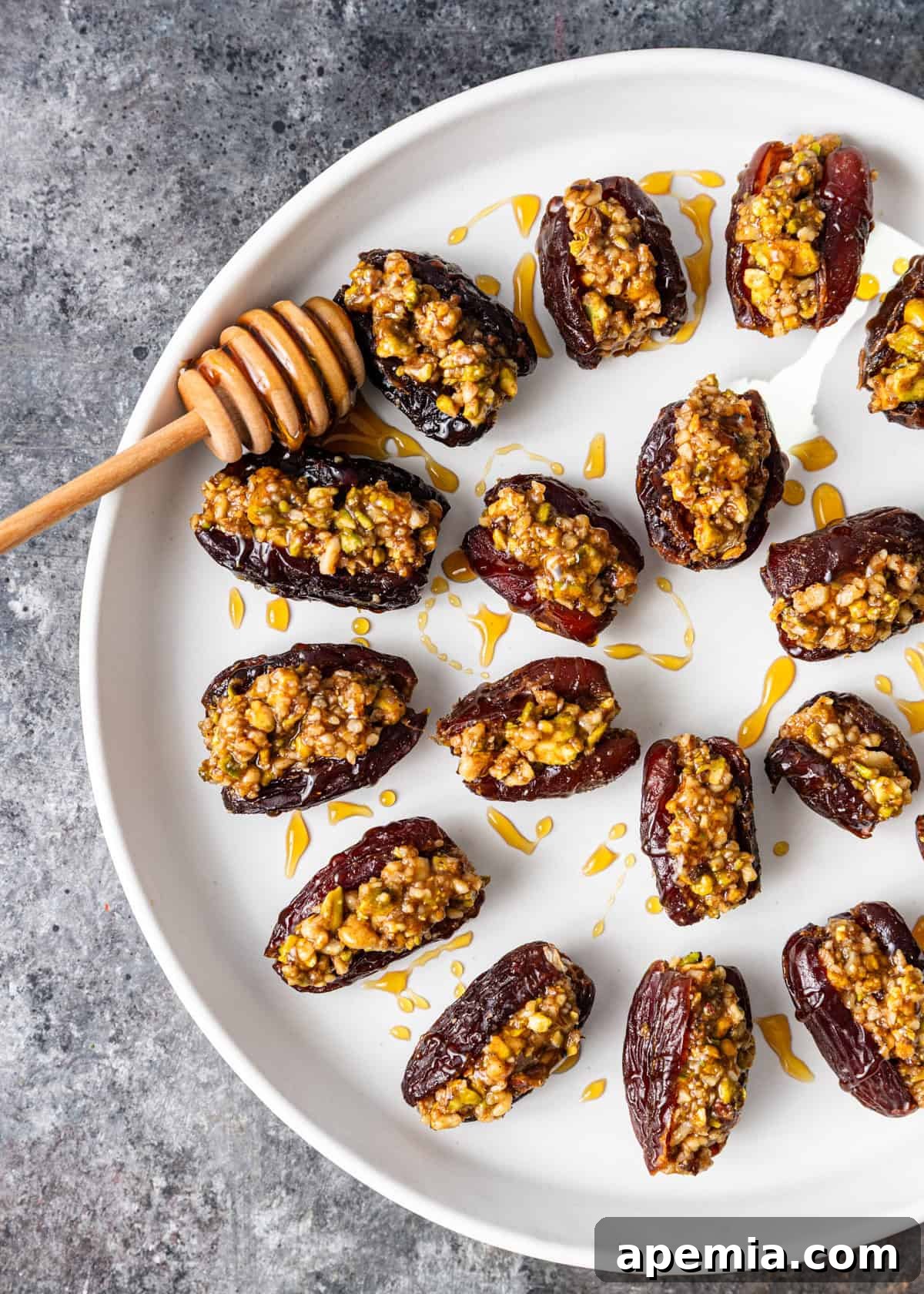 Overhead view: a white plate brimming with artfully arranged Baklava Stuffed Dates, generously drizzled with golden honey.