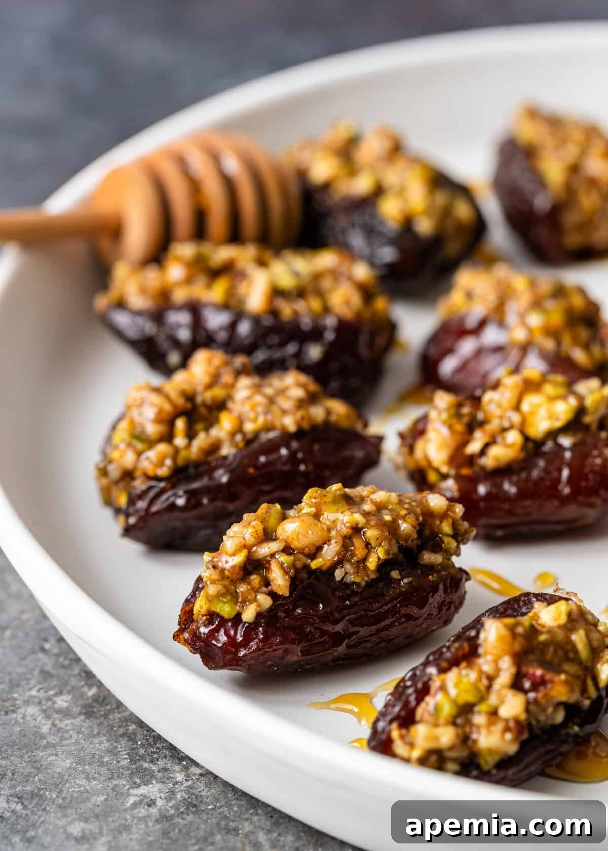Closeup side view: an artfully arranged stack of Baklava Stuffed Dates on a white plate, showcasing their rich filling and a generous drizzle of honey on top.