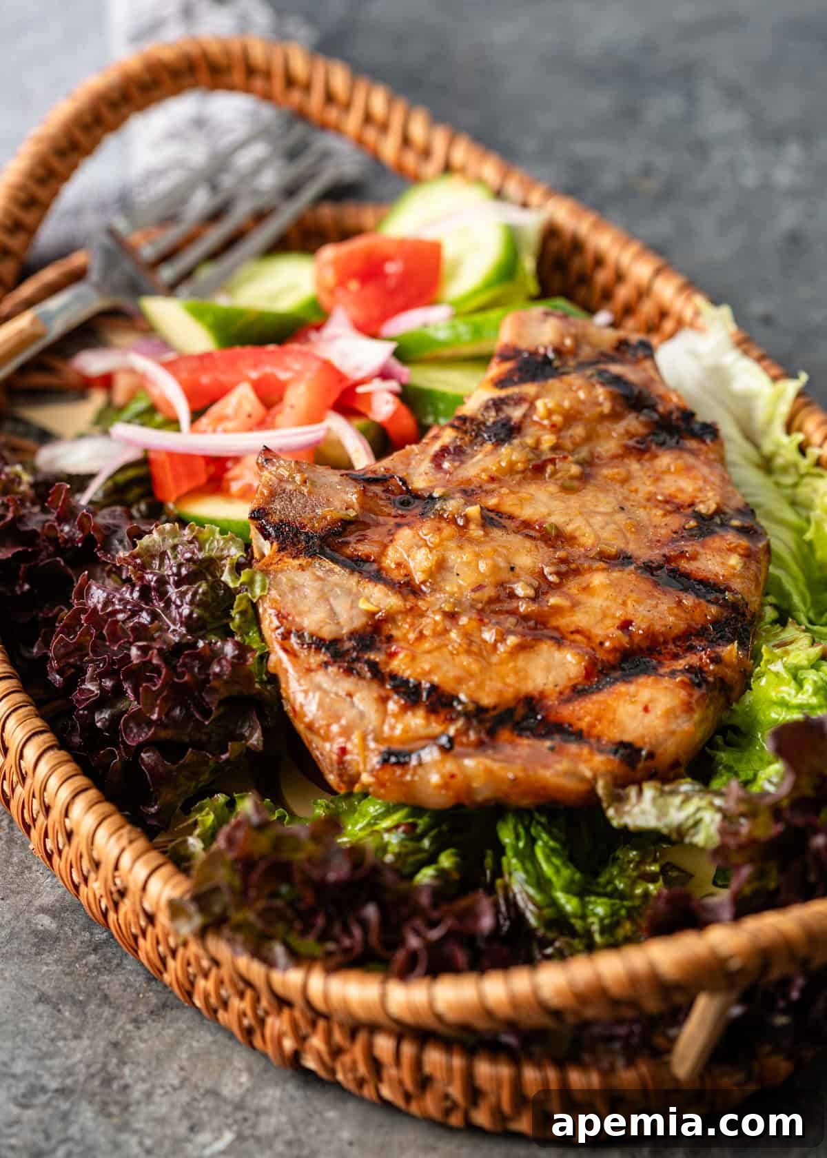 Overhead close-up of Vietnamese pork chops served atop a bed of fresh greens in a charming wicker basket serving tray, with a fork resting beside it.