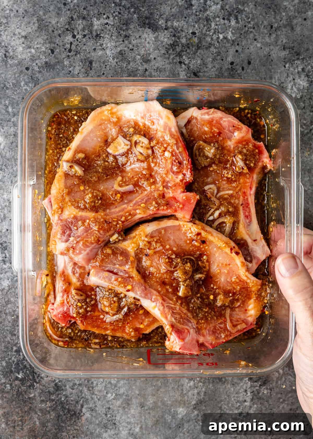 Overhead process shot showing the vibrant marinade ingredients expertly mixed and coating the pork chops in a clear bowl, sitting on a kitchen counter, ready for marination.