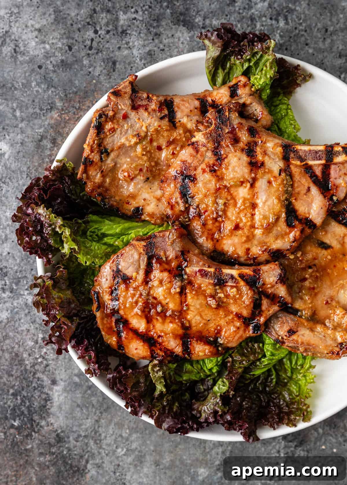 Overhead close-up of perfectly cooked Sườn Nướng (Vietnamese Pork Chops) elegantly presented over a bed of fresh lettuce on a crisp white plate.