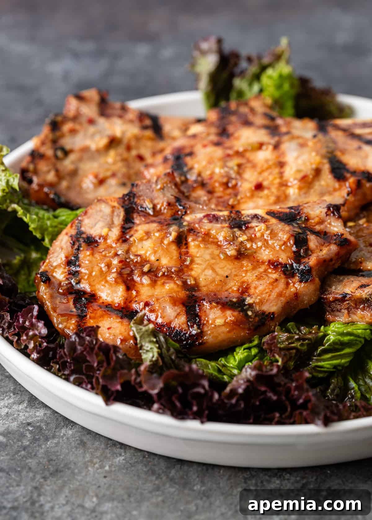 Close-up side view of succulent Vietnamese pork chops, cooked to perfection and served over a bed of fresh lettuce on a white plate, showcasing their inviting caramelization.