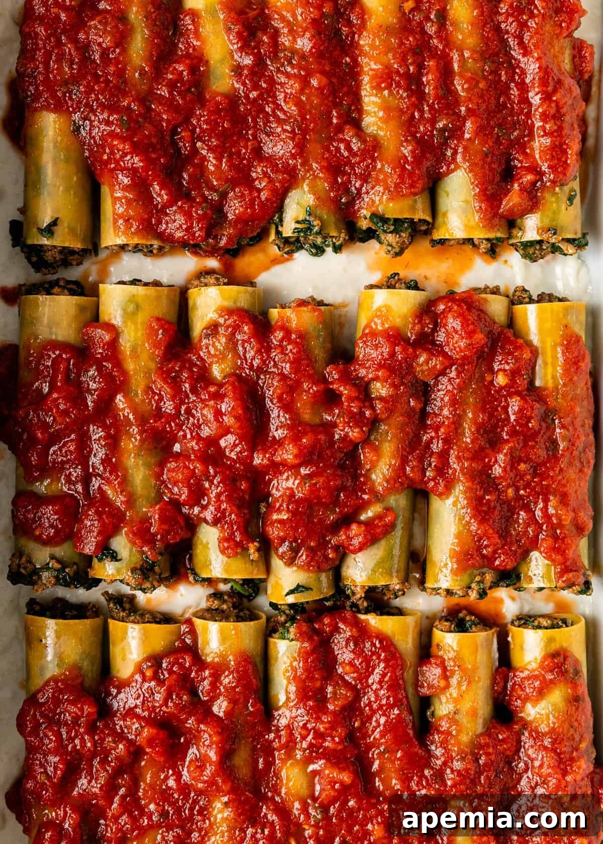 overhead process shot: cannelloni shell with the prepared meat filling on sheet pan with tomato sauce on top