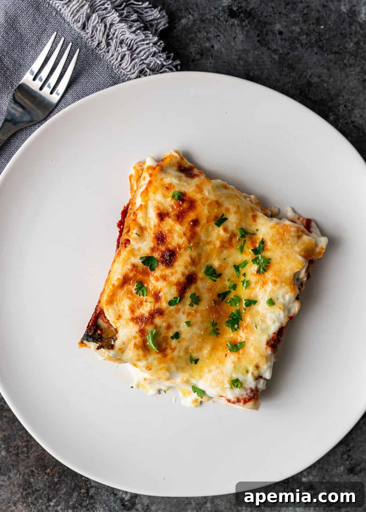 overhead: slice of cannelloni on white plate with fork off to side