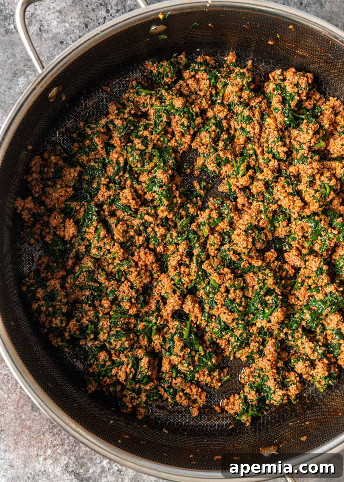 overhead process shot: beef mixture in skilled with spinach and seasonings mixed together