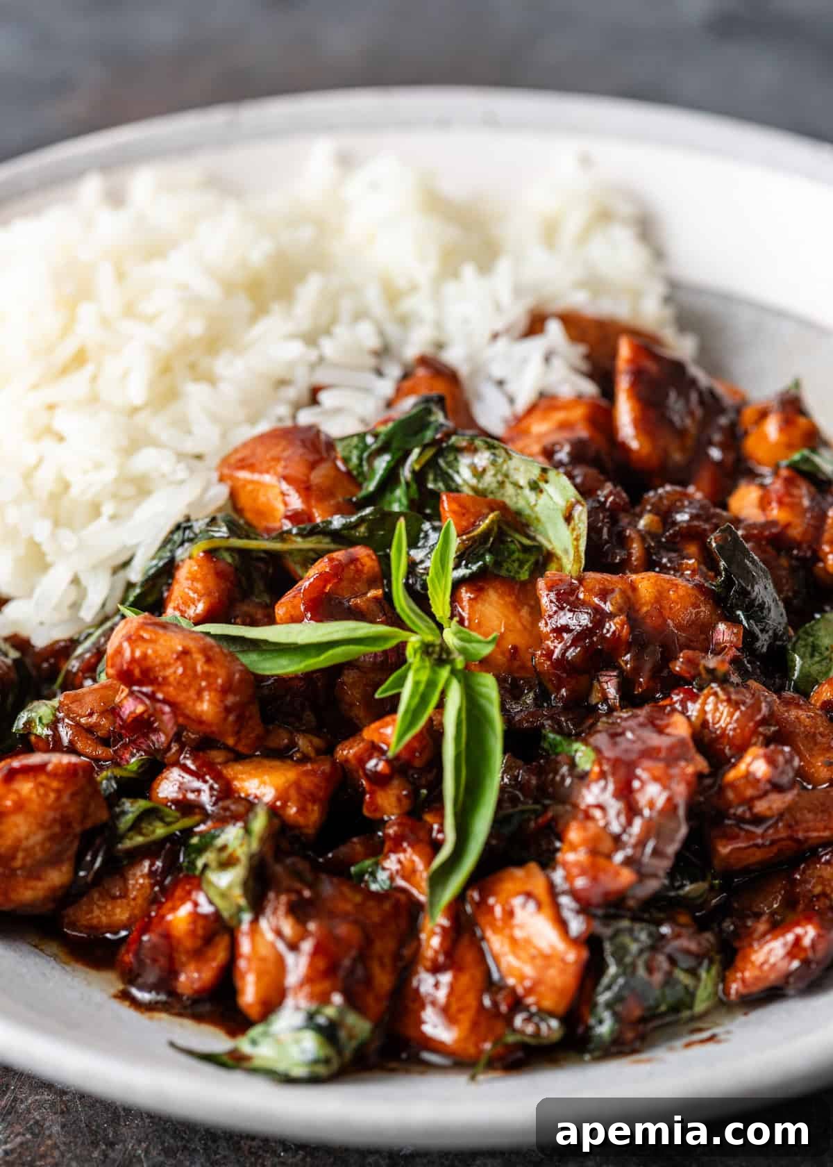 Side view of a serving of Thai Basil Chicken with white rice on a white plate, showcasing the succulent chicken and fresh basil.