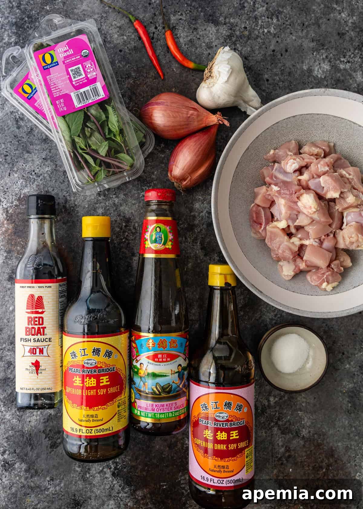 Overhead view of all fresh ingredients laid out on a wooden surface, ready for making Thai Basil Chicken, including chicken, basil, chilies, and sauces.
