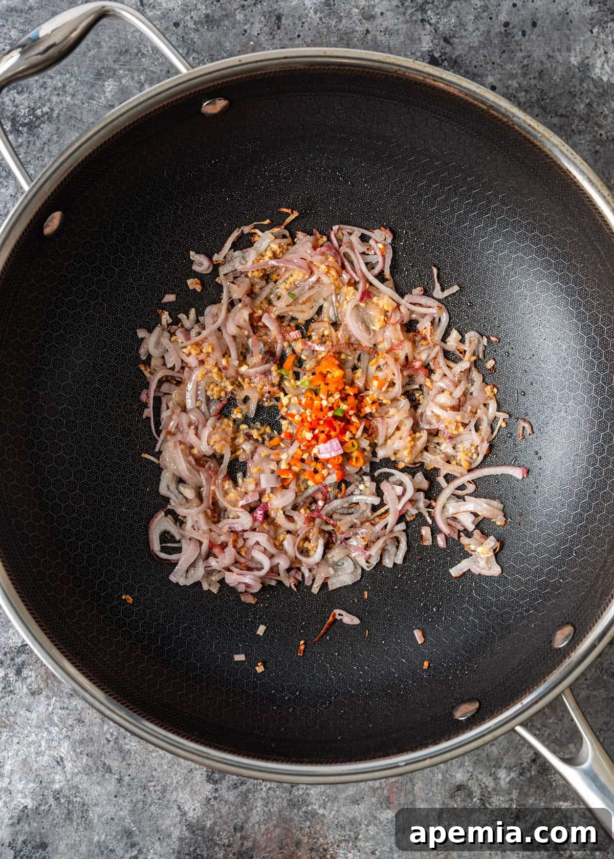 Process shot: Garlic, shallots, and Thai chilies sizzling in a hot wok with oil, releasing their fragrant aromas.