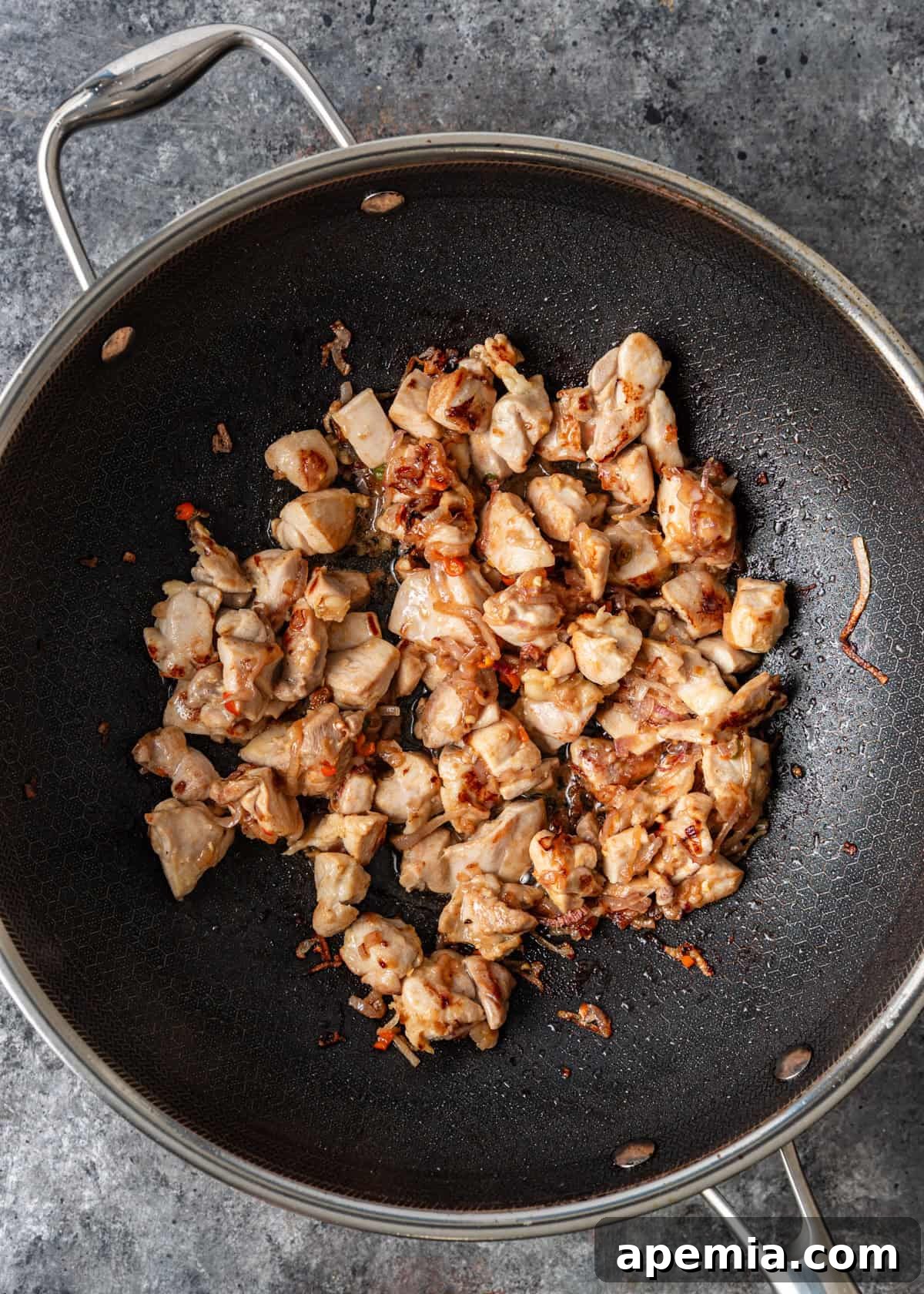 Process shot: Cubed chicken thighs added to the wok with sautéed aromatics, beginning to cook and brown.