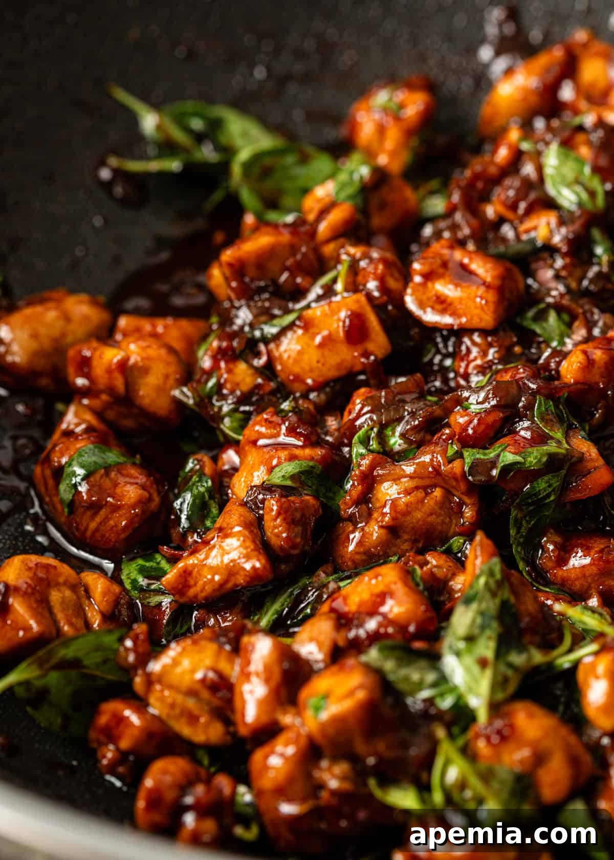 A close-up of a perfectly cooked Thai Basil Chicken dish on a white plate, showcasing the vibrant colors of the basil and chicken.