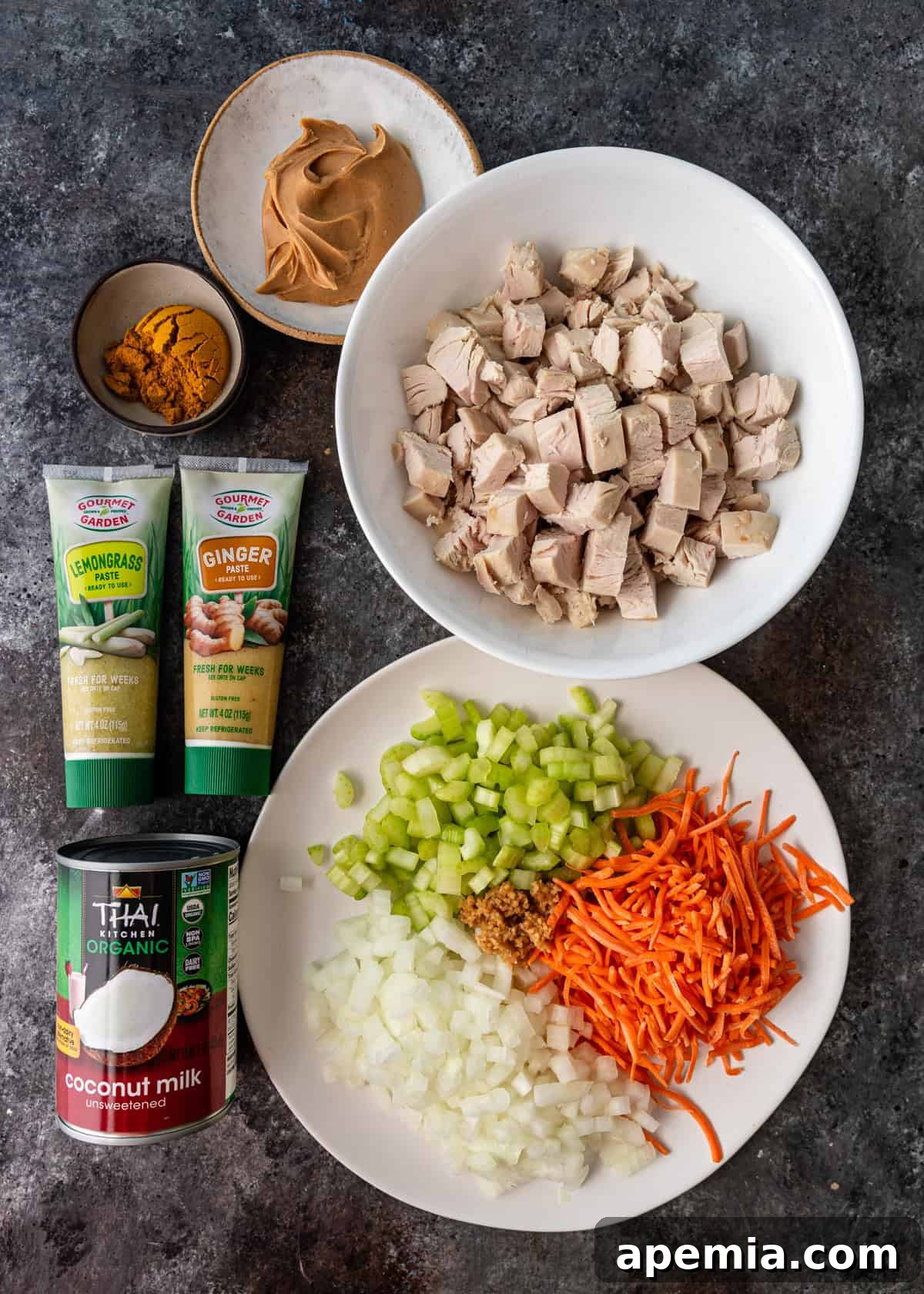Overhead shot of all the fresh ingredients laid out on a wooden surface, ready to make the homemade peanut curry recipe, including chicken, vegetables, spices, coconut milk, and peanut butter.